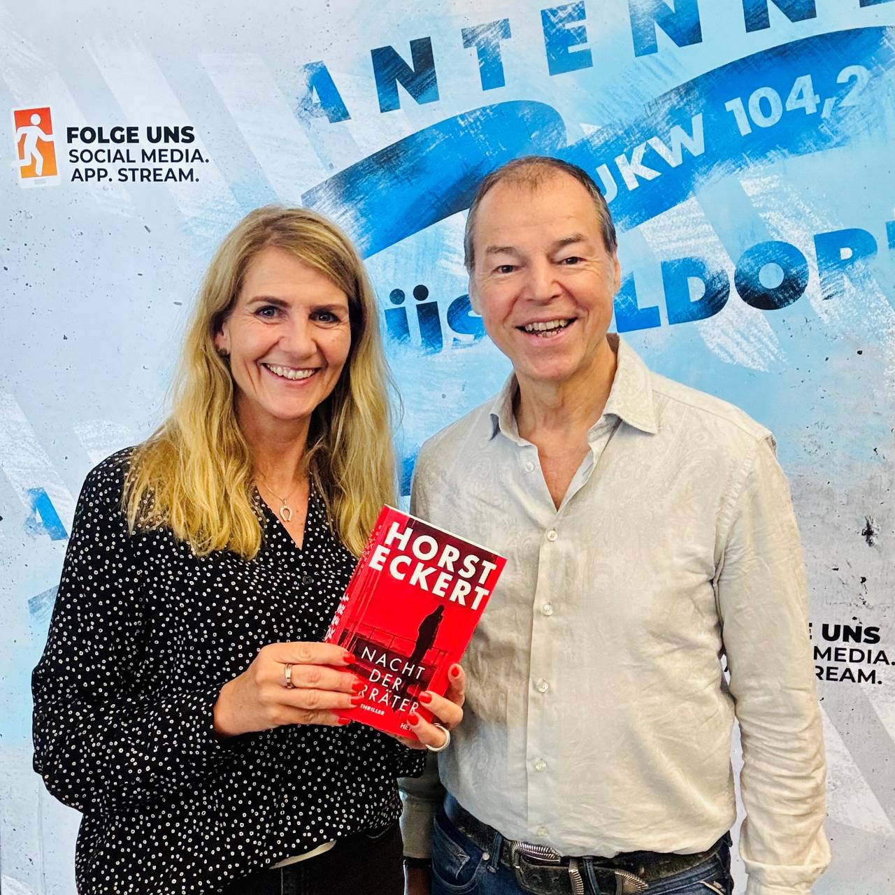 Moderatorin Claudia Monréal mit ihrem Talkgast Horst Eckert vor der Social Media Wand von Antenne Düsseldorf