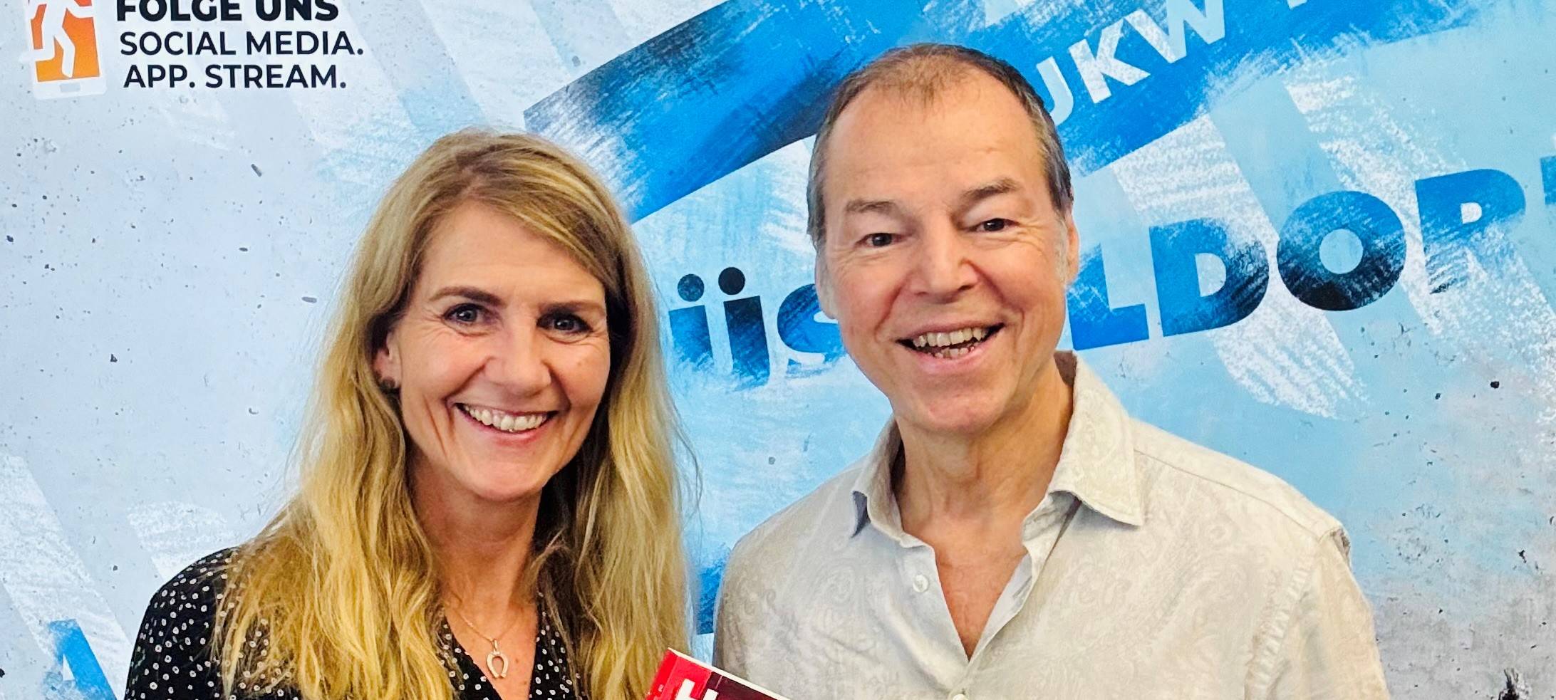 Moderatorin Claudia Monréal mit ihrem Talkgast Horst Eckert vor der Social Media Wand von Antenne Düsseldorf