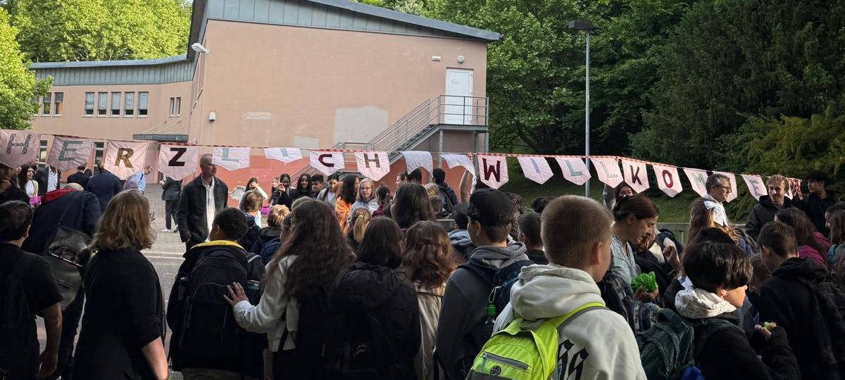 Die Schülerinnen und Schüler aus Erkrath laufen durch das Schultor, darüber hängt der Schriftzug Herzlichen Willkommen.