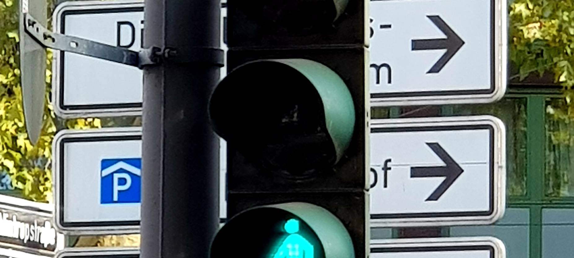 Eine normale Ampel leuchtet grün. Im Hintergrund sind mehrere Schilder zu sehen.
