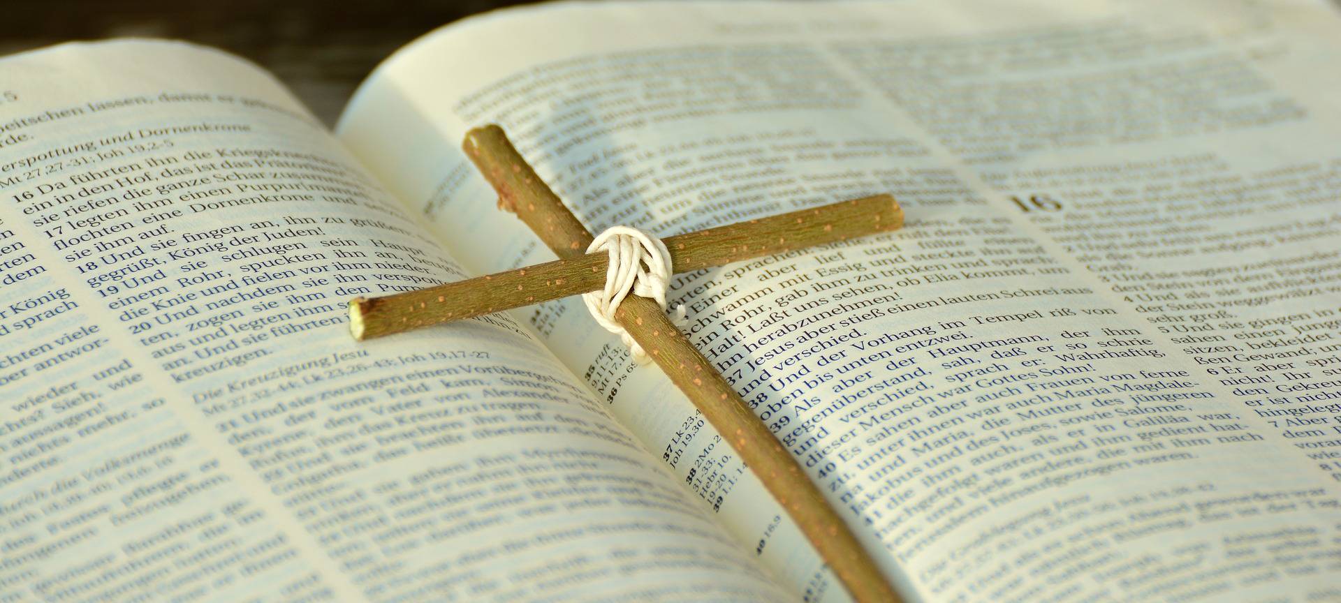 Ein schlichtes Holzkreuz liegt auf einer geöffneten Bibel.