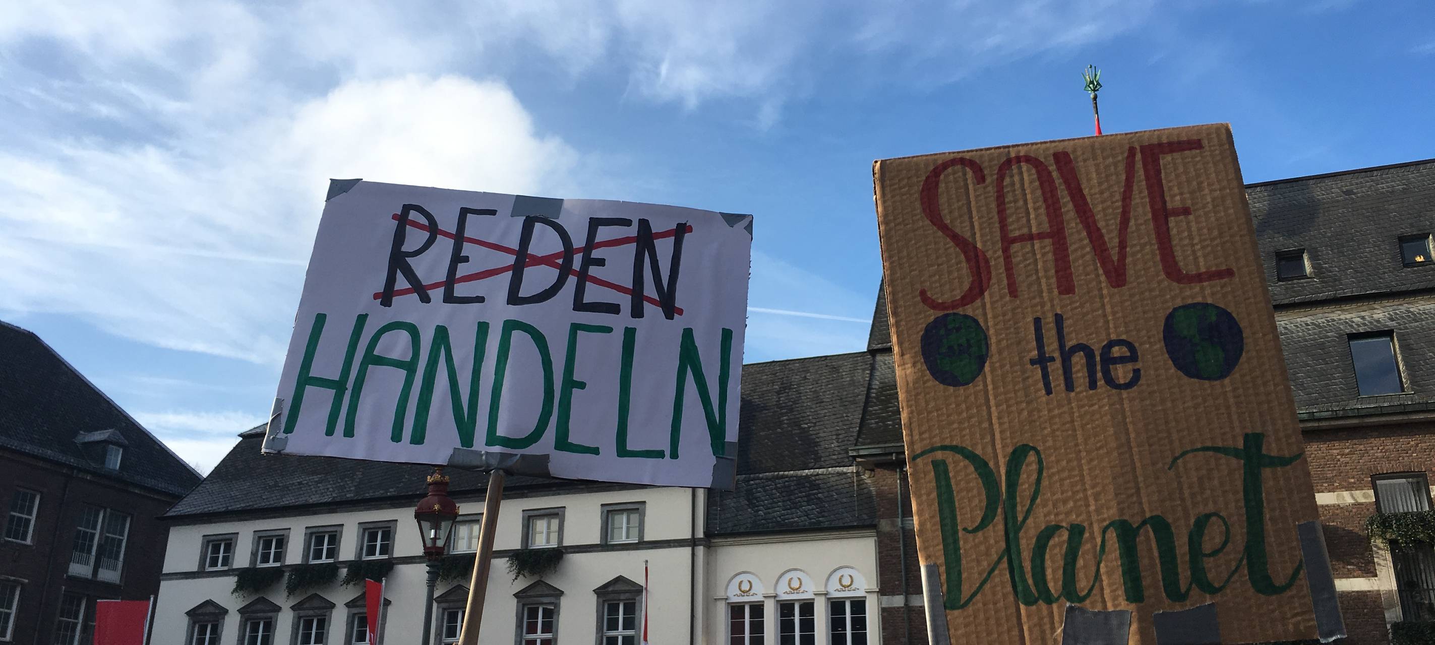 Zwei Demo-Plakate zum Thema Klimaschutz. "Reden" ist durchgestrichen, stattdessen ist "Handeln" zu lesen. "Save the planet" steht auf einem weiteren Plakat.