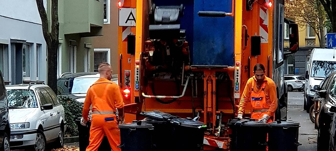 Zwei Mitarbeiter der Awista heben Mülltonnen in einem Müllwagen.