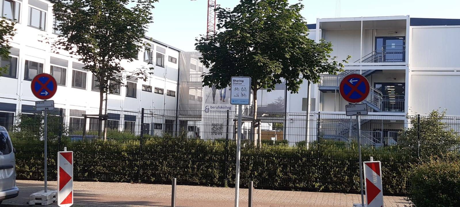 Im Vordergrund ein abgesperrter Parkplatz, an dem ein Schild mit der Info "Sharing-Station"