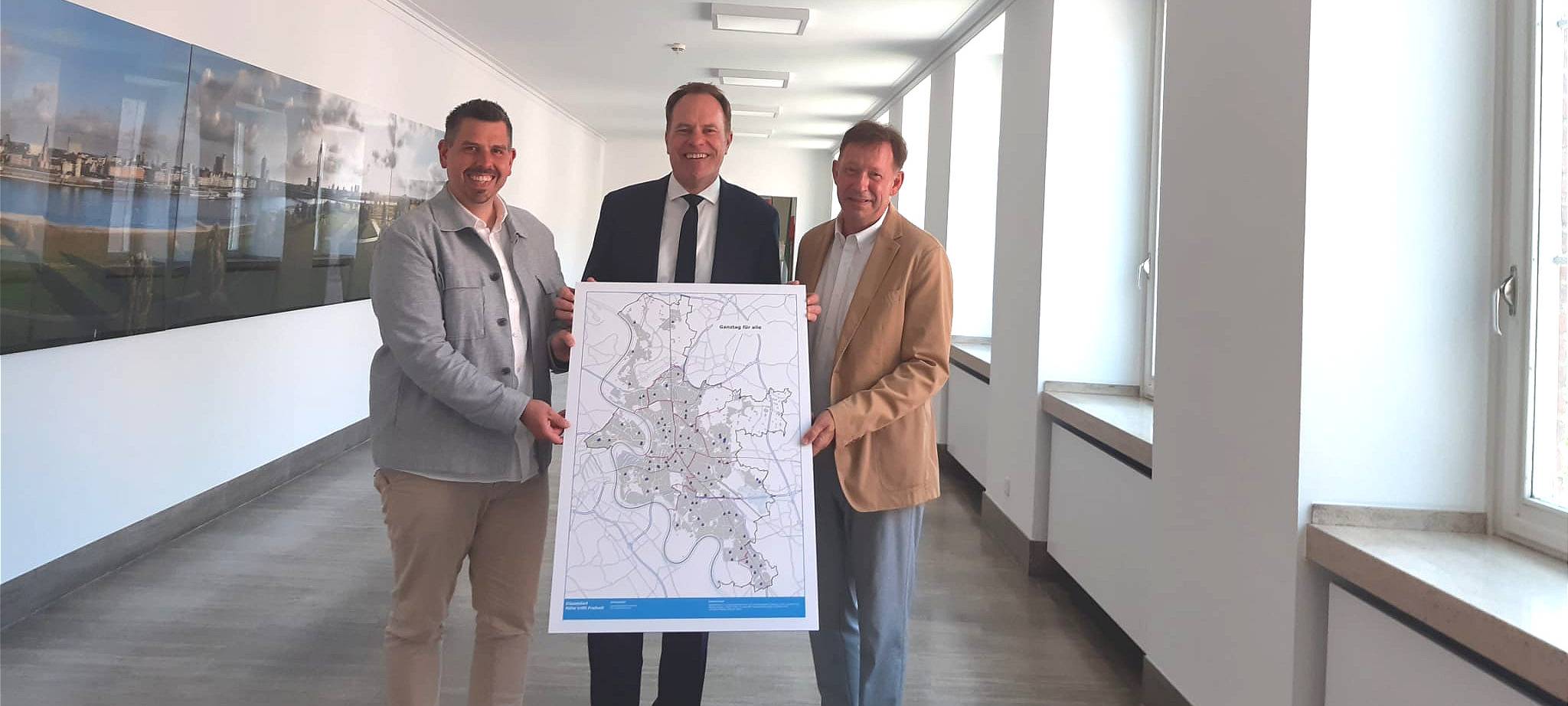 Drei Männer stehen in einem Flur und halten ein Plakat hoch, auf dem die Stadtkarte von Düsseldorf zu sehen ist.