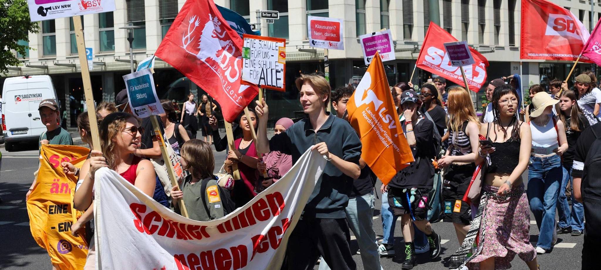 ine Gruppe Schüler*innen demonstriert, sie halten Banner und Schilder hoch und laufen über eine Straße.