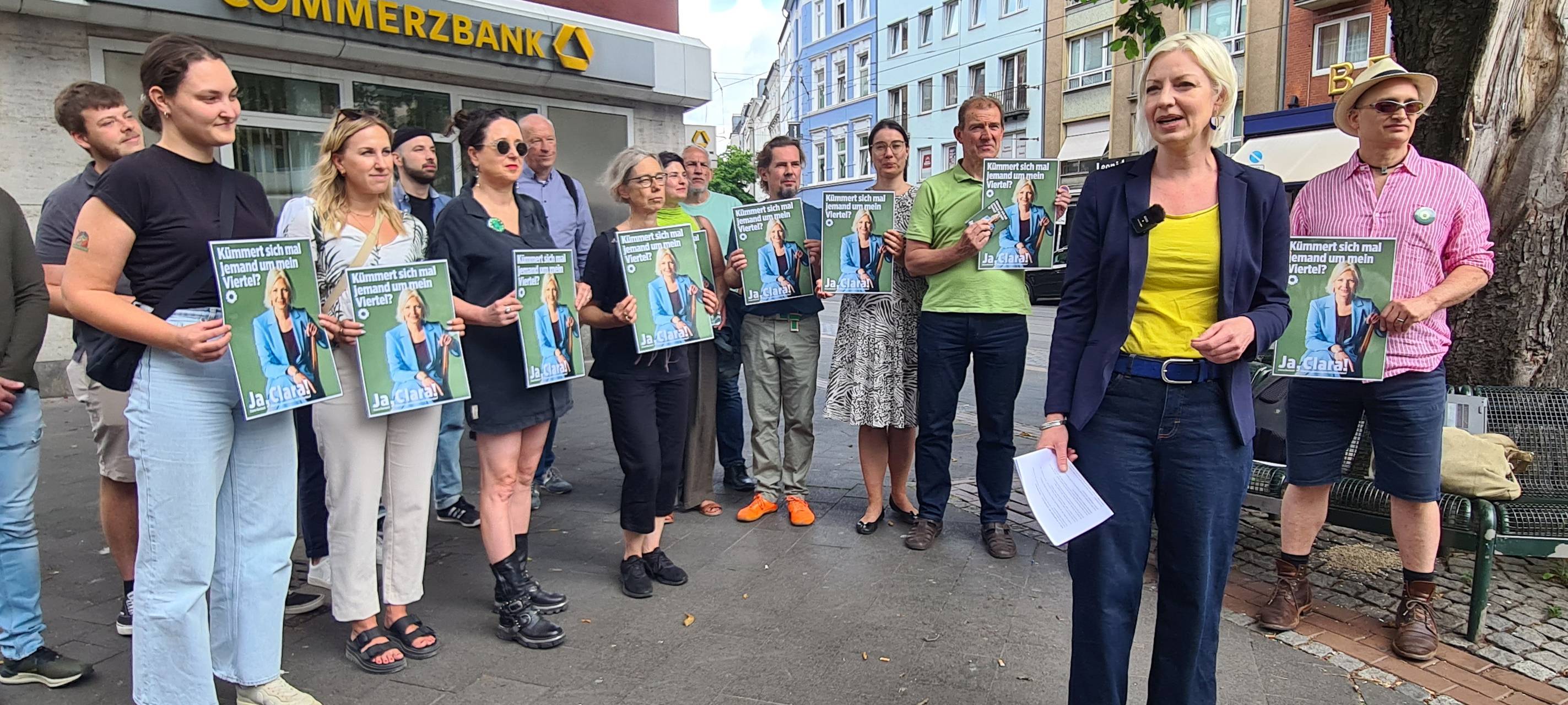 Eine Gruppe Menschen steht im Halbkreis um die Grünen-Politikerin Clara Gerlach, alle halten Schilder hoch.