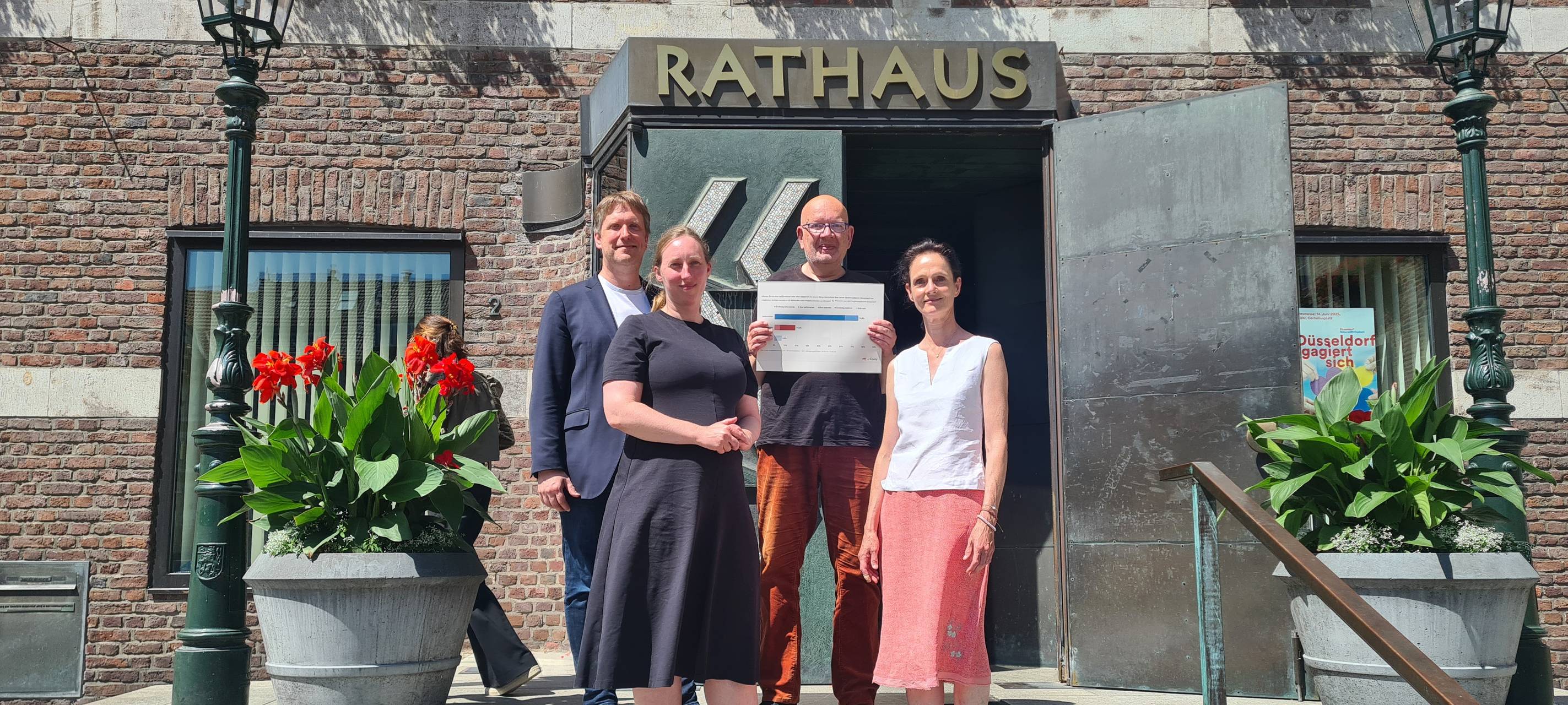 Vier Menschen stehen auf den Stufen vor der Eingangstür zum Düsseldorfer Rathaus. Einer hält ein Schild in den Händen.