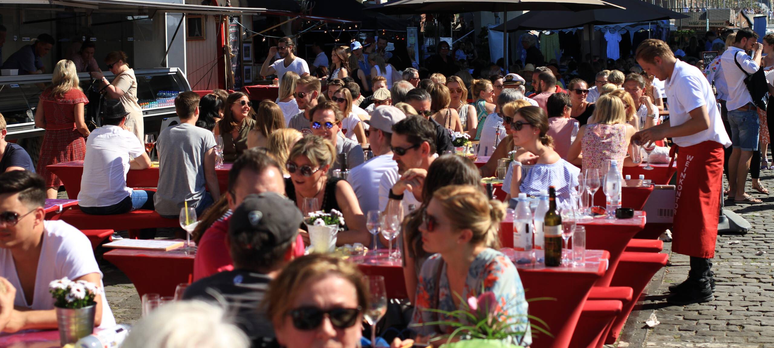 Viele Menschen sitzen gemeinsam gemütlich an Tischen beim Düsseldorfer Fischmarkt.