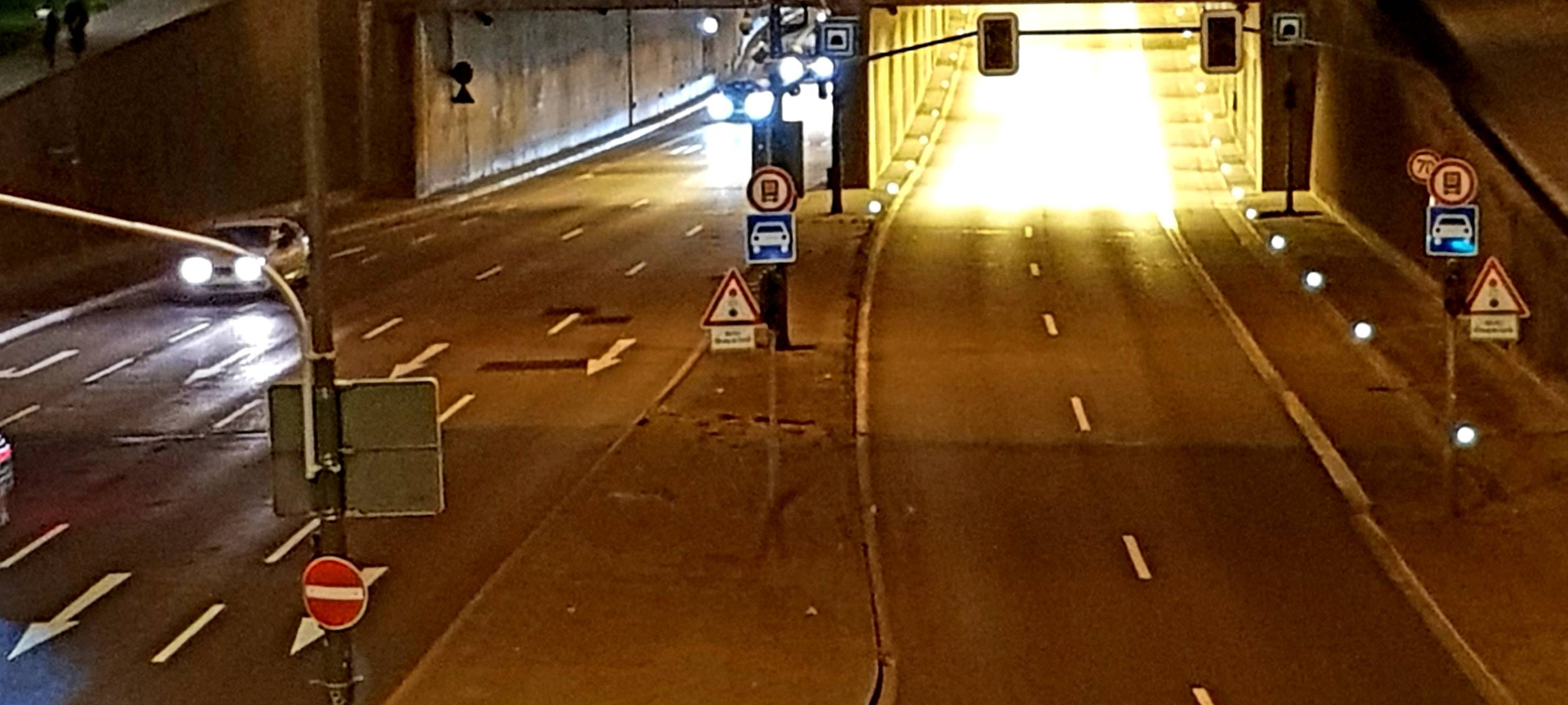 Ein Bild bei Nacht zeigt den Rheinufertunnel. Auf der linken Seite sind Autos und Scheinwerfer zu sehen. Die rechte Röhre des Tunnels ist Autofrei.