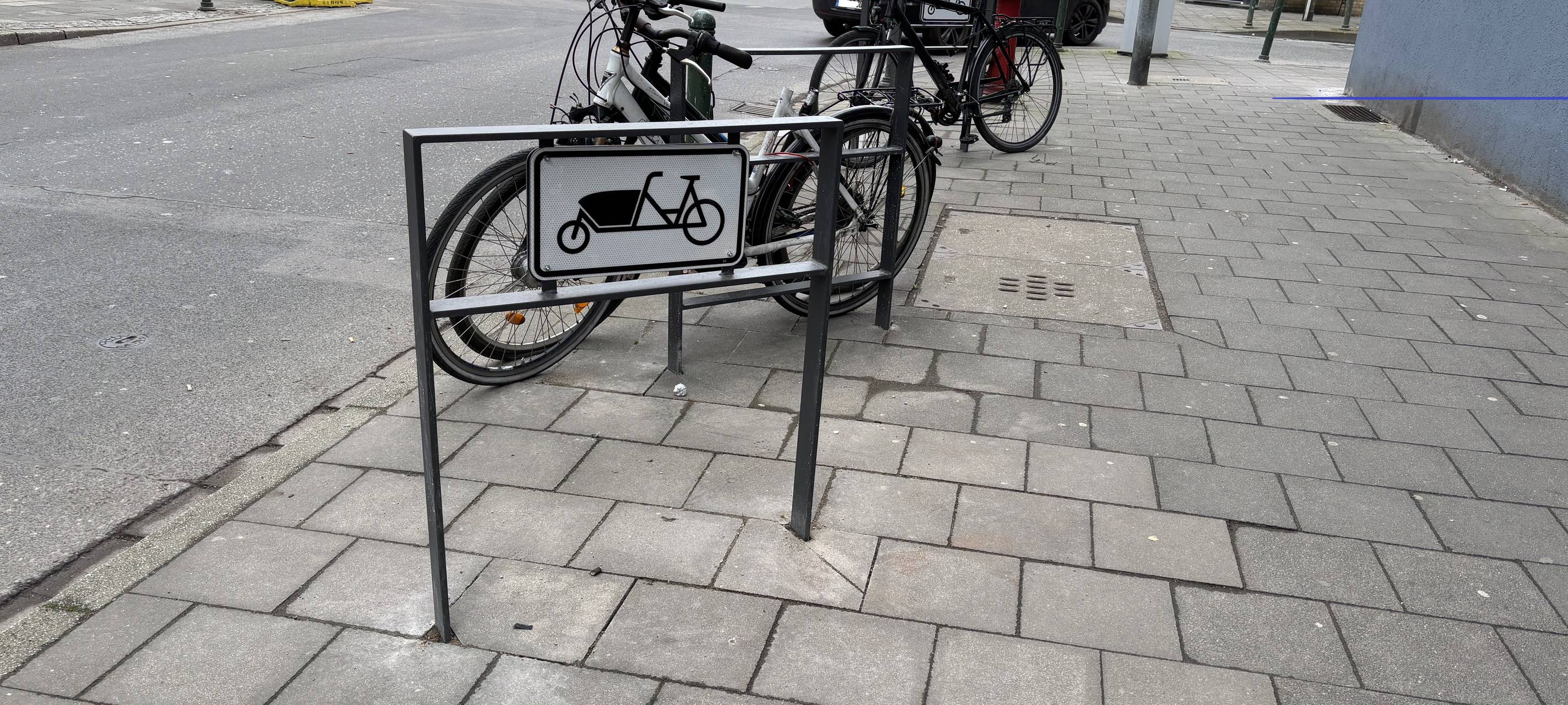 Ein Fahrradbügel auf der Luisenstraße. Im Hintergrund stehen zwei angeschlossene Fahrräder.