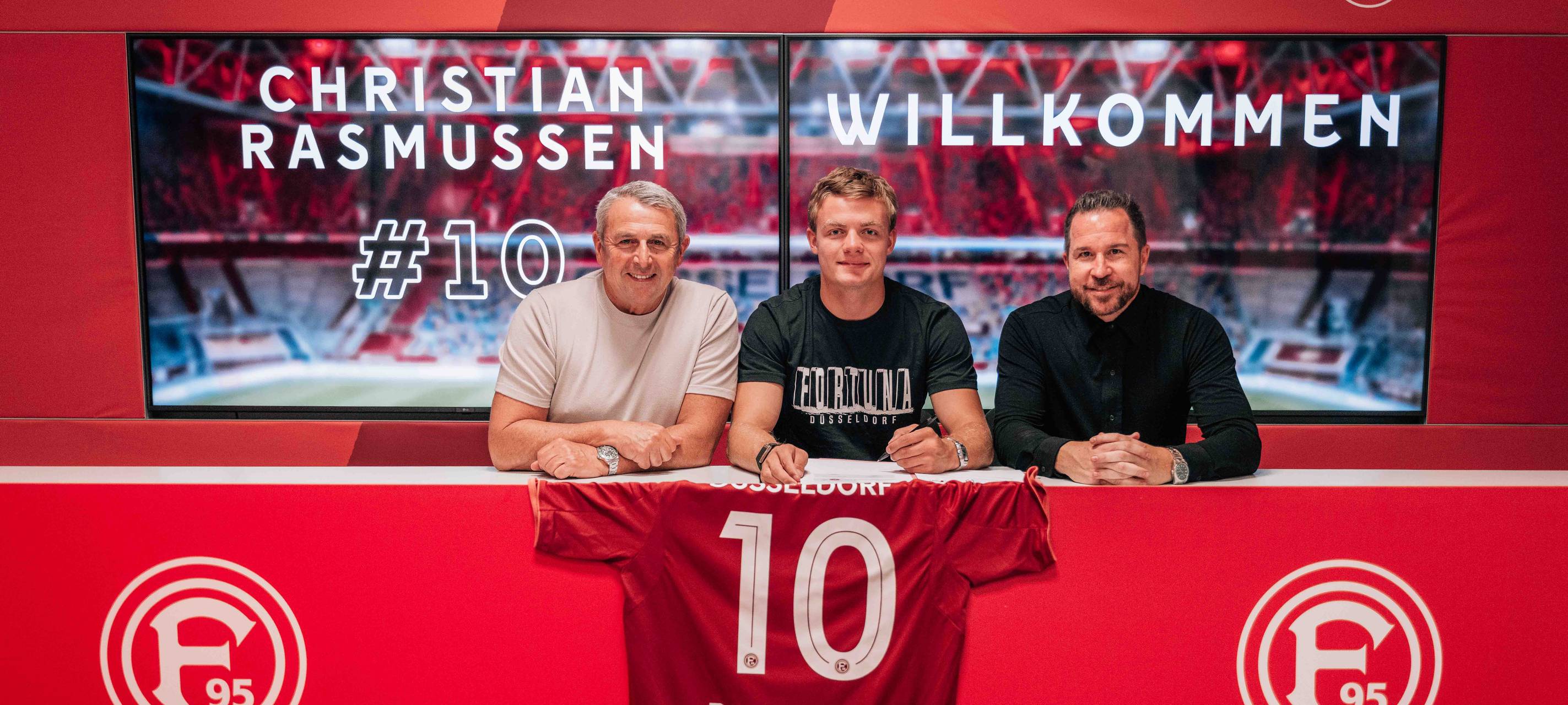 Der neue Spieler Christian Rasmussen sitzt zwischen zwei Männern und unterschreibt seinen Vertrag.