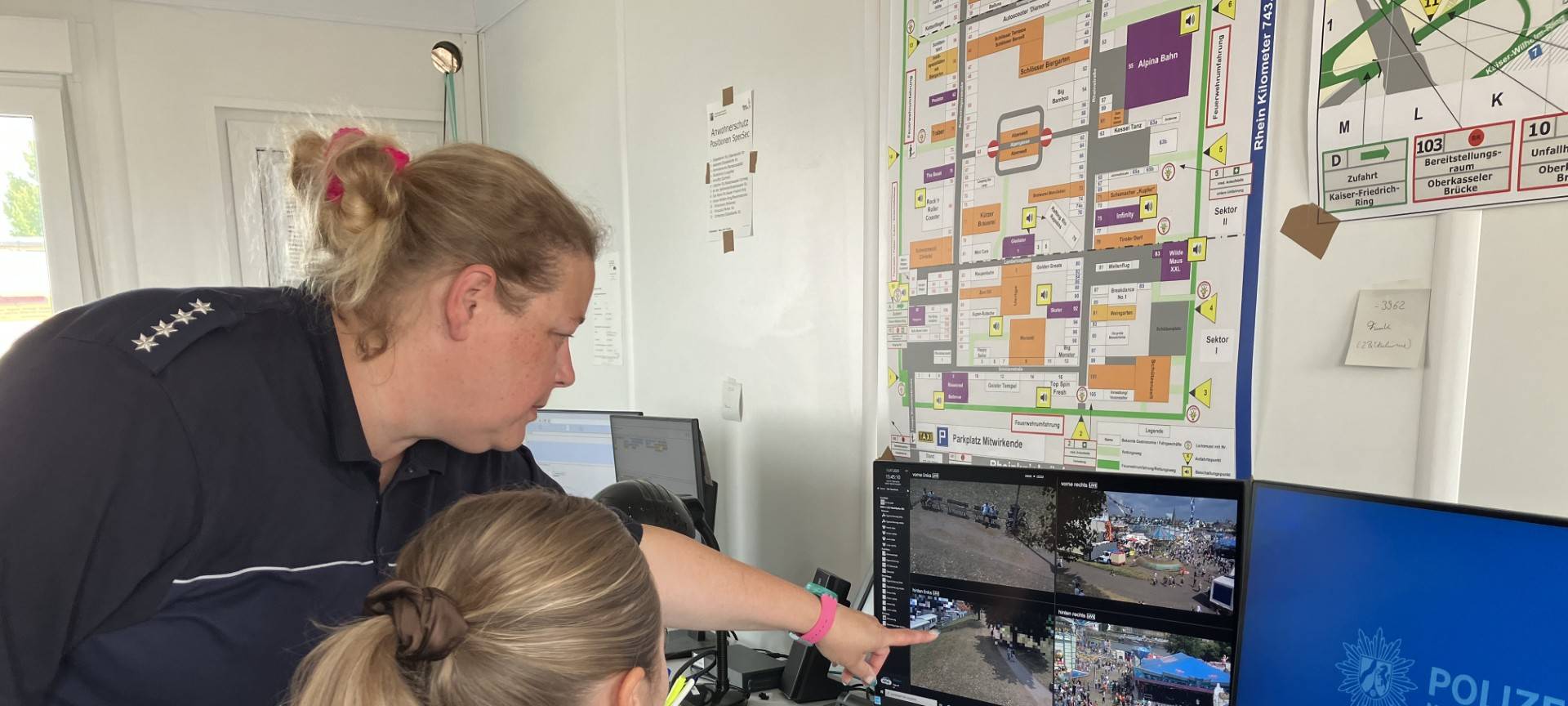 Zwei Polizistinnen schauen auf einen viergeteilten Bildschirm, der Bilder einer Überwachungskamera von der Düsseldorfer Rheinkirmes zeigt.
