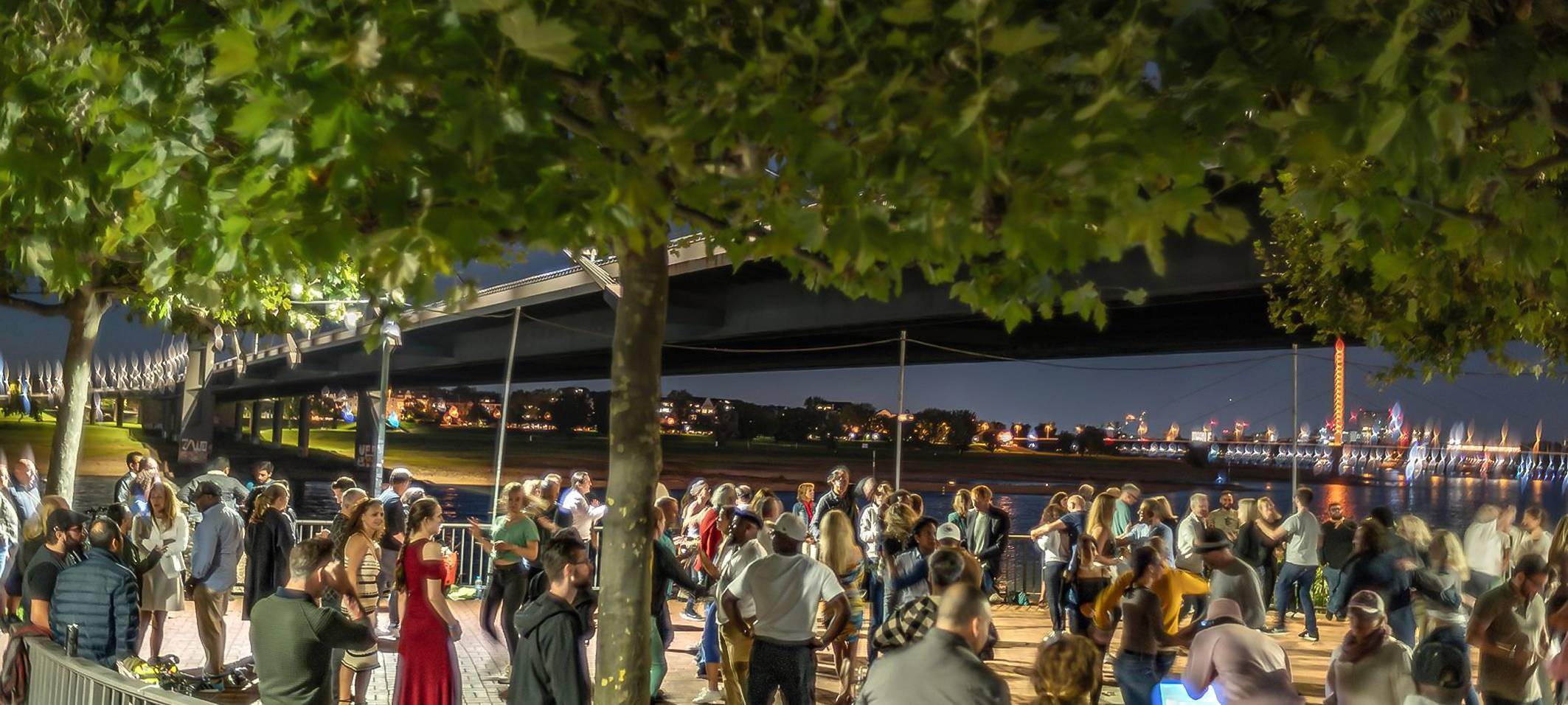 Viele Menschen tanzen in der Nähe der Kniebrücke Salsa unter freiem Himmel. Im Hintergrund sind die Lichter der Rheinkirmes zu sehen.