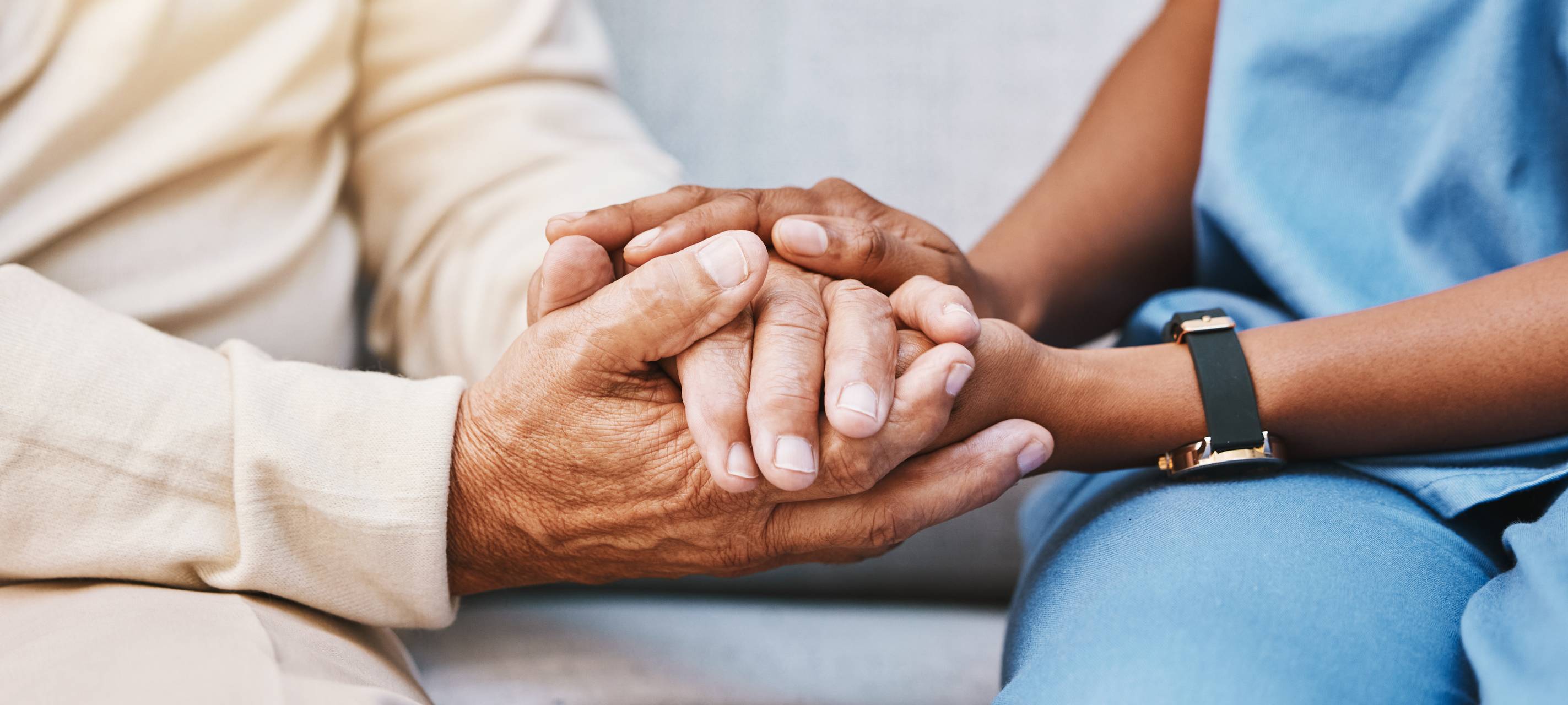 Eine Pflegerin hält die Hände einer älteren Person.