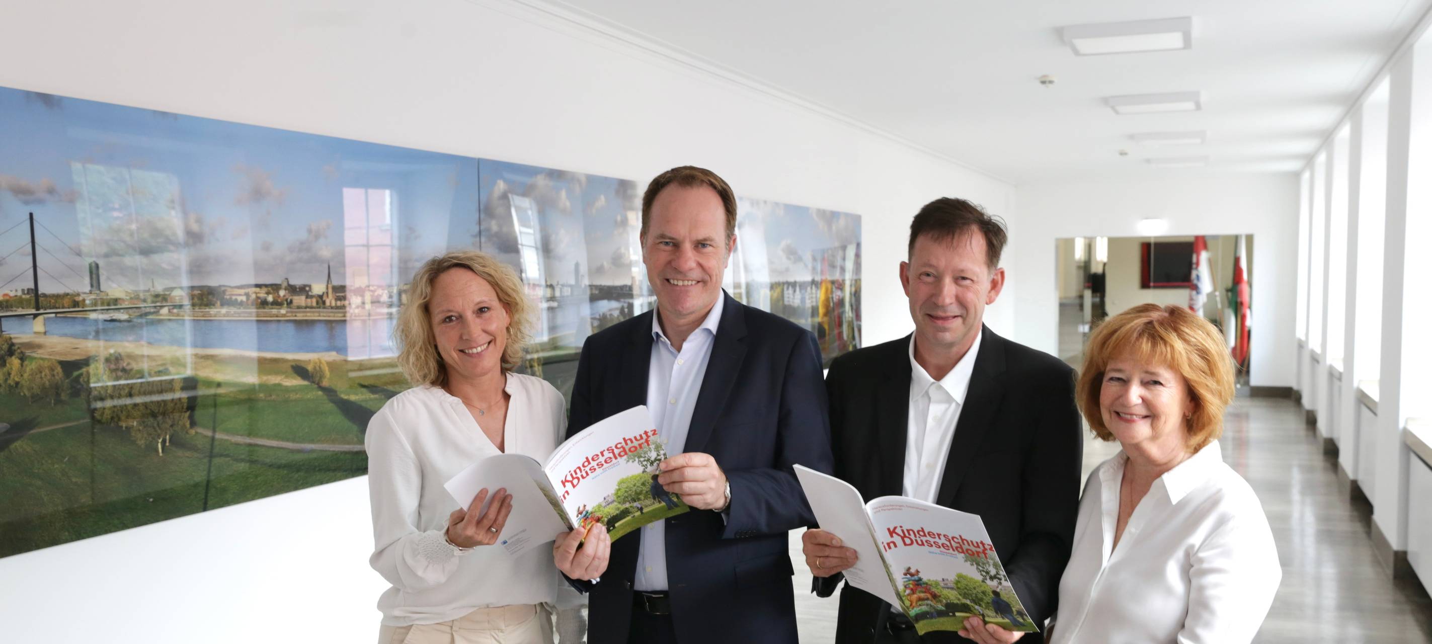 Daniela Schmitt, Sachgebietsleitung 24-Stunden Kinderschutzdienst, Oberbürgermeister Dr. Stephan Keller, Stadtdirektor Burkhard Hintzsche, und Renate Schäfer-Sikora, stellvertretende Leiterin des Amtes für Soziales und Jugend stehen im Rathaus und halten die neue Broschüre "Kinderschutz in Düsseldorf" in der Hand.