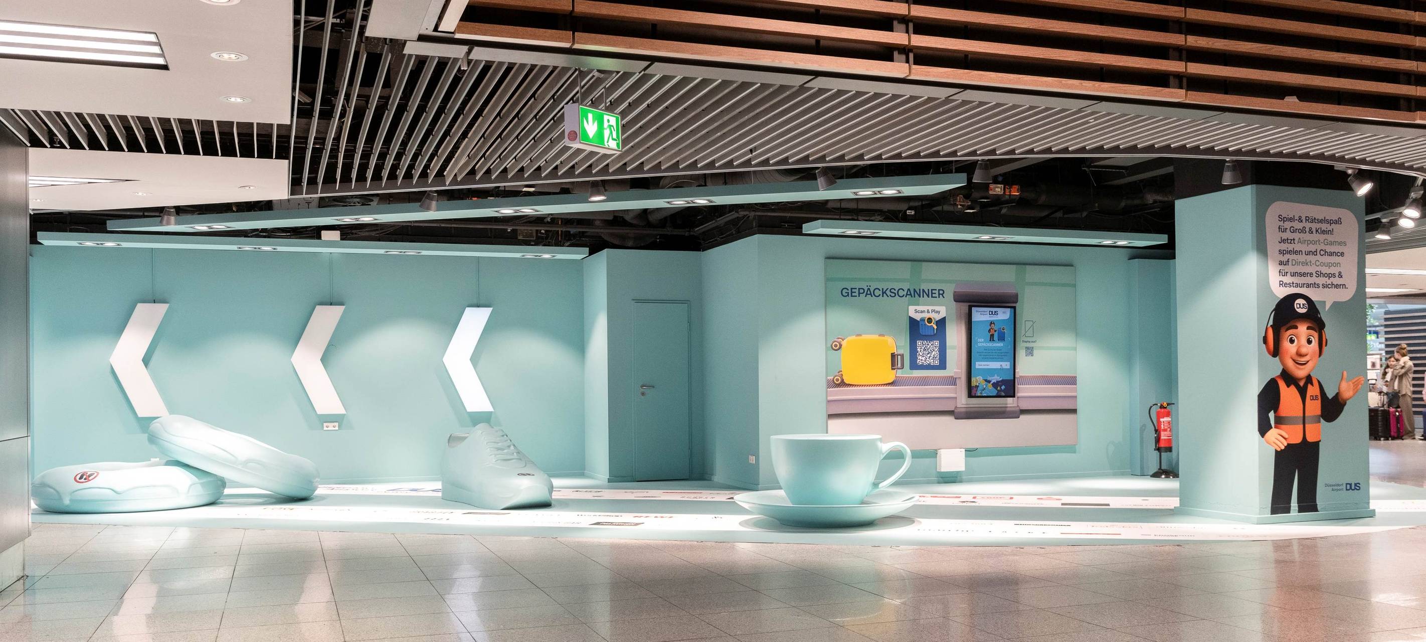 Ein Bereich am Flughafen an dem Besucher Selfies machen und Spiele spielen können. Unter anderem sind übergroße Turnschuhe und eine Kaffeetasse zu sehen.