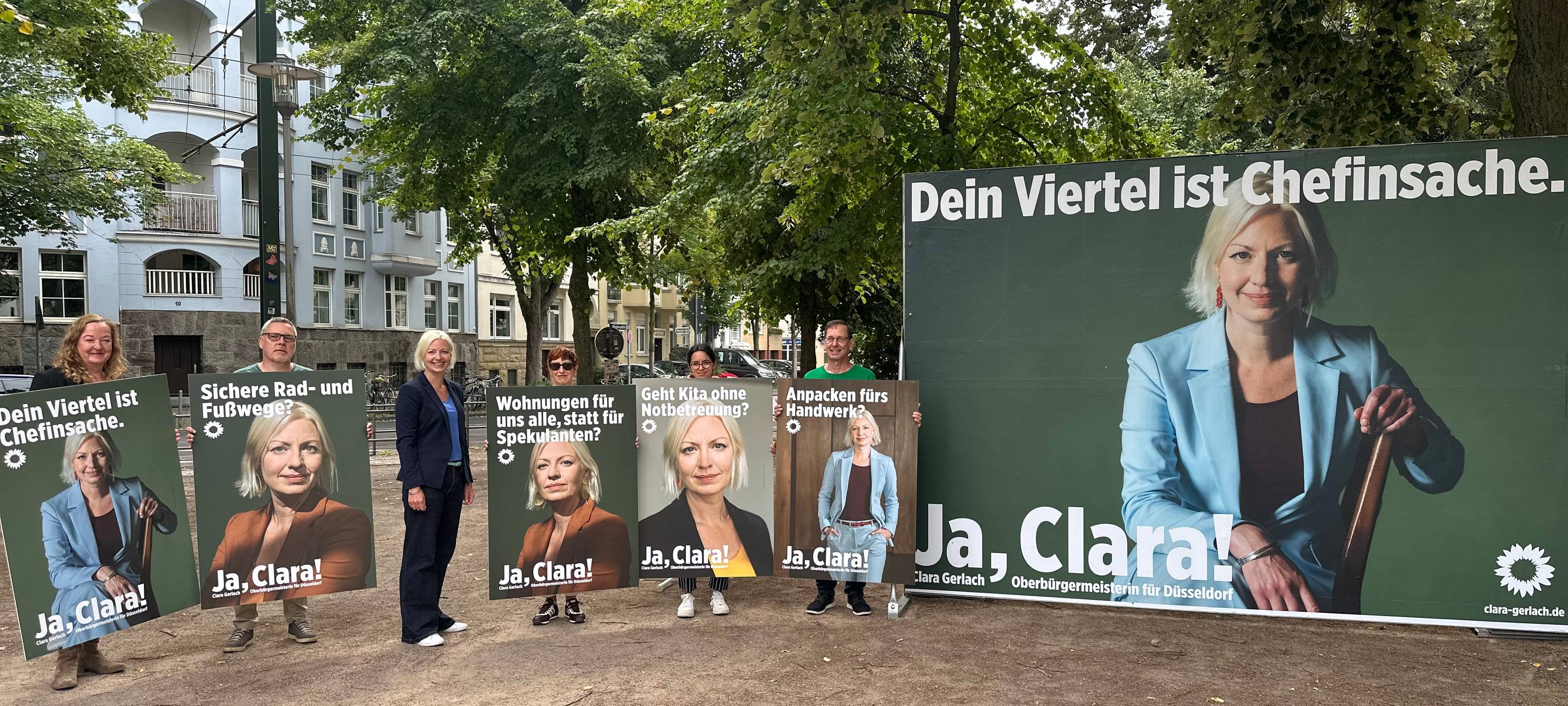 Oberbürgermeister-Kandidatin Clara Gerlach steht zwischen ihren Wahlplakaten, auf denen jeweils Clara Gerlach zu sehen ist. Daneben ein Großplakat der Kampagne.