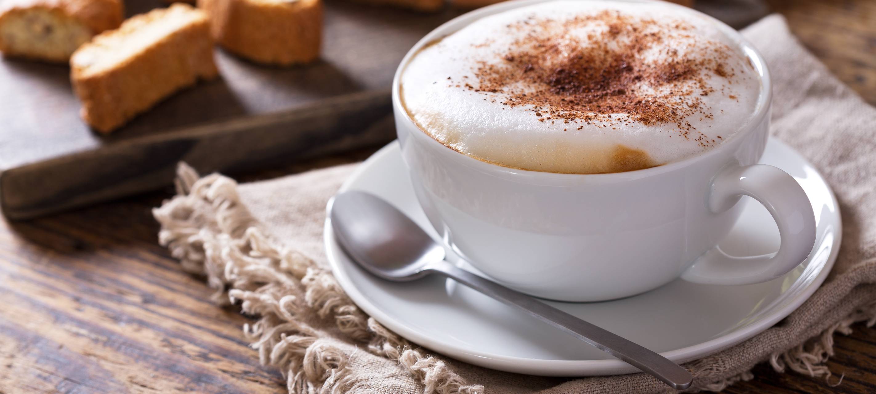 Ein servierter Cappuccino mit Kakao-Pulver. Auch Cantuccini werden serviert.