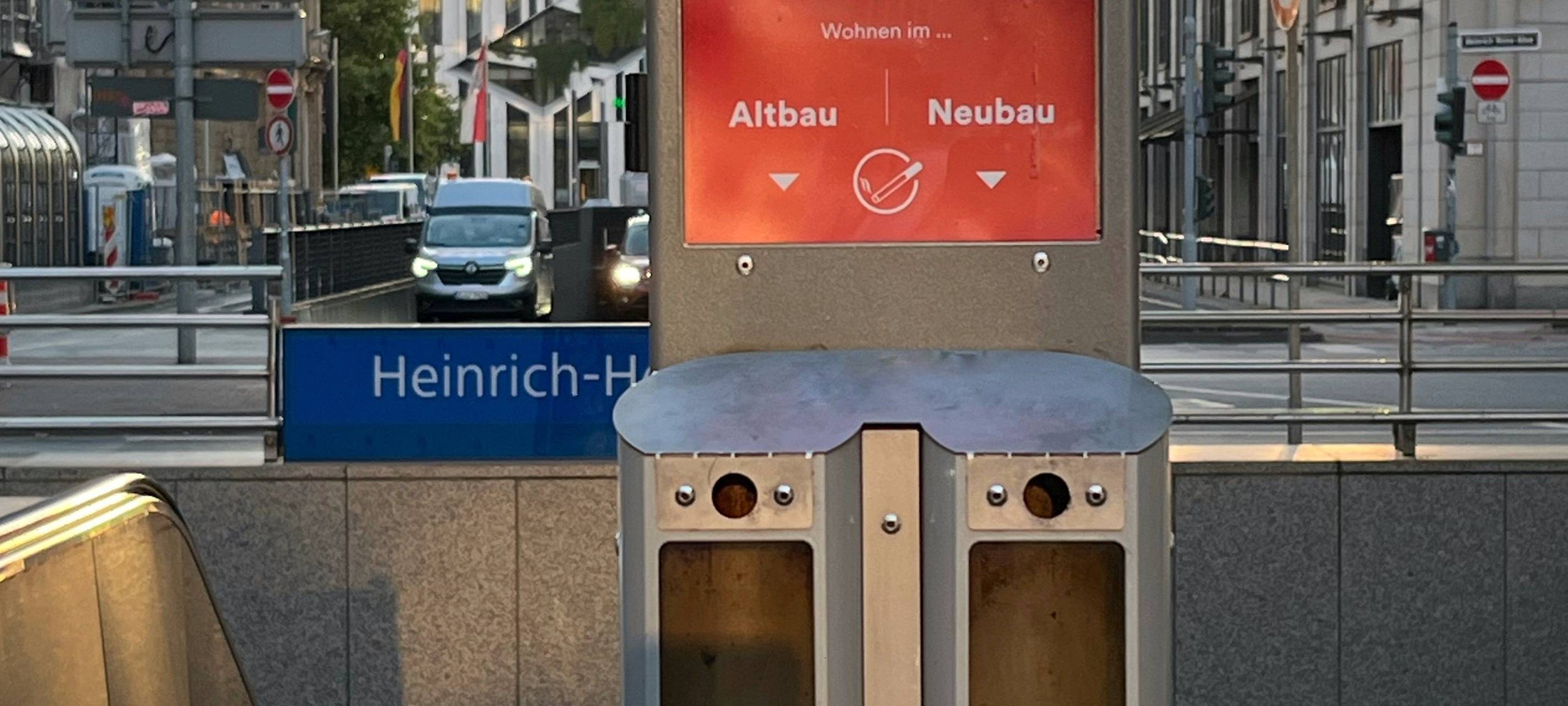 Abstimm-Aschenbecher am Eingang zur U-Bahnstation Heinrich-Heine-Allee. Im Hintergrund Hochhäuser und die Straße in Richtung Könisallee.