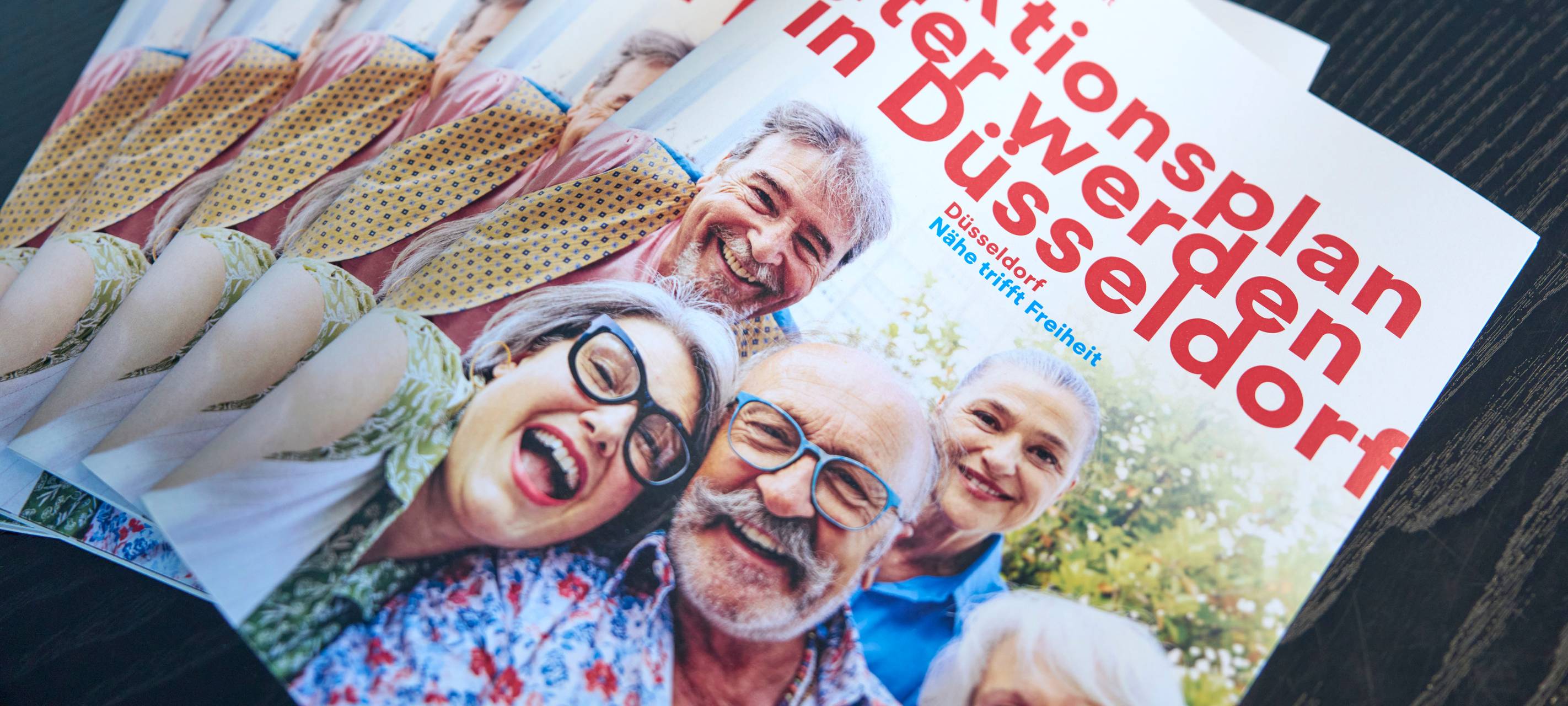 Mehrere Broschüren vom Aktionsplan "Älter werden in Düsseldorf" liegen auf einem Tisch.