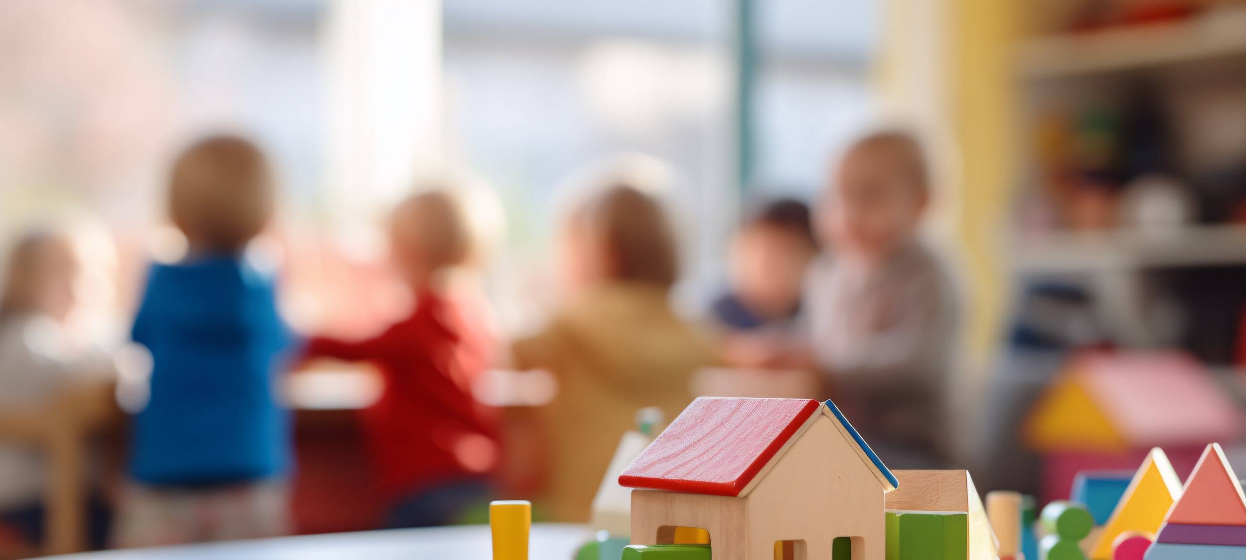 Bausteinspielzeug und unscharf spielende Kinder im Hintergrund in einer Kindertagesstätte, einem Kindergarten oder einer Vorschule