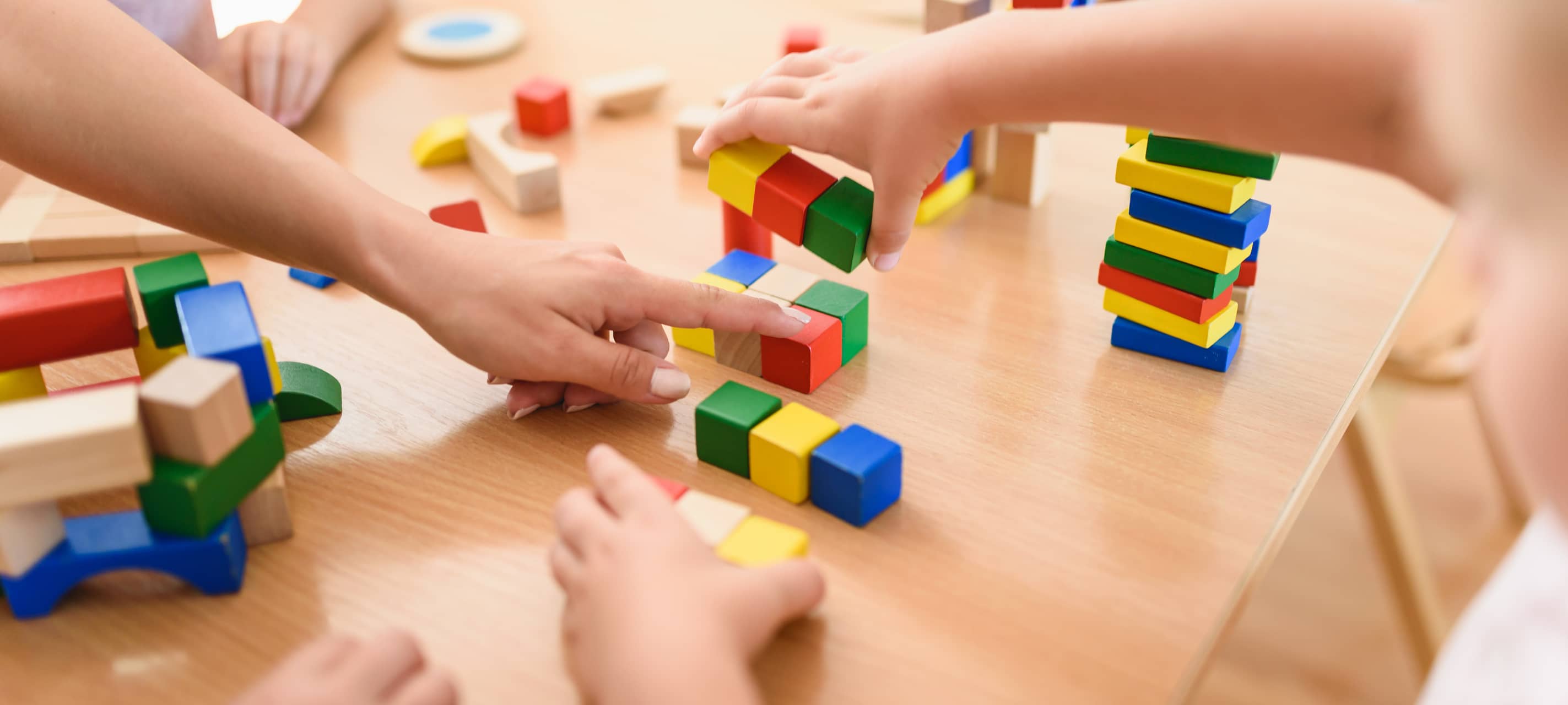 Vorschullehrerin mit Kindern, die im Kindergarten mit buntem, didaktischem Holzspielzeug spielen.