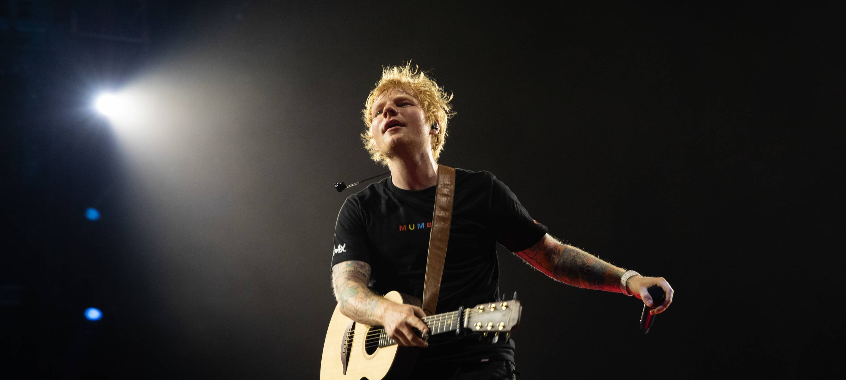 Ed Sheeran performet auf einer Bühne. Dabei wird er von einem Scheinwerfer angeleuchtet.