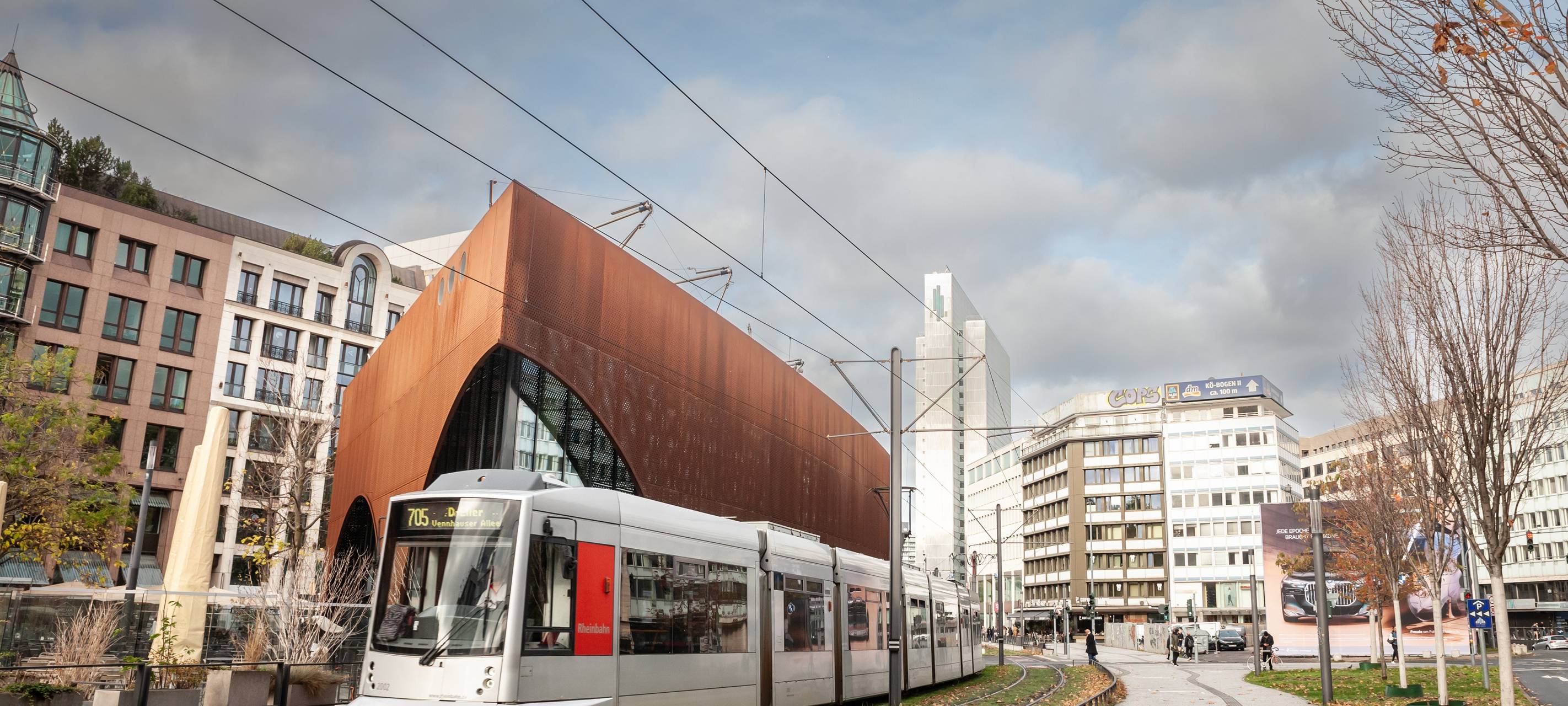 Eine Straßenbahn der Düsseldorfer Straßenbahn fährt durch das Stadtzentrum von Düsseldorf. Die Bahn wird von der Rheinbahn betrieben und ist Teil des öffentlichen Nahverkehrs. Im Hintergrund sind städtische Gebäude und Passanten zu sehen.