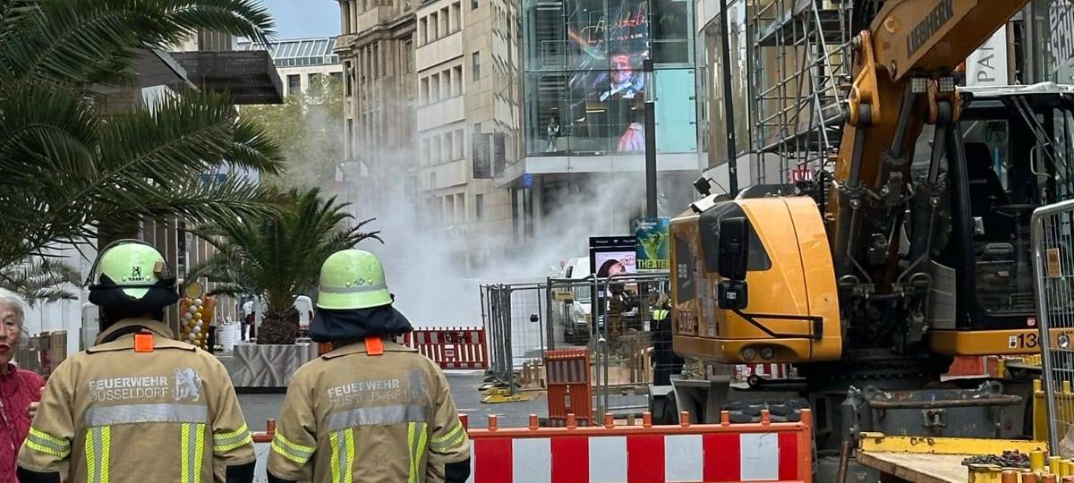 Der Bereich rund um einen Bagger auf der Schadowstraße ist abgesperrt. Feuerwehrleute sind dort im Einsatz. Auf der Straße ist Rauch zu sehen.
