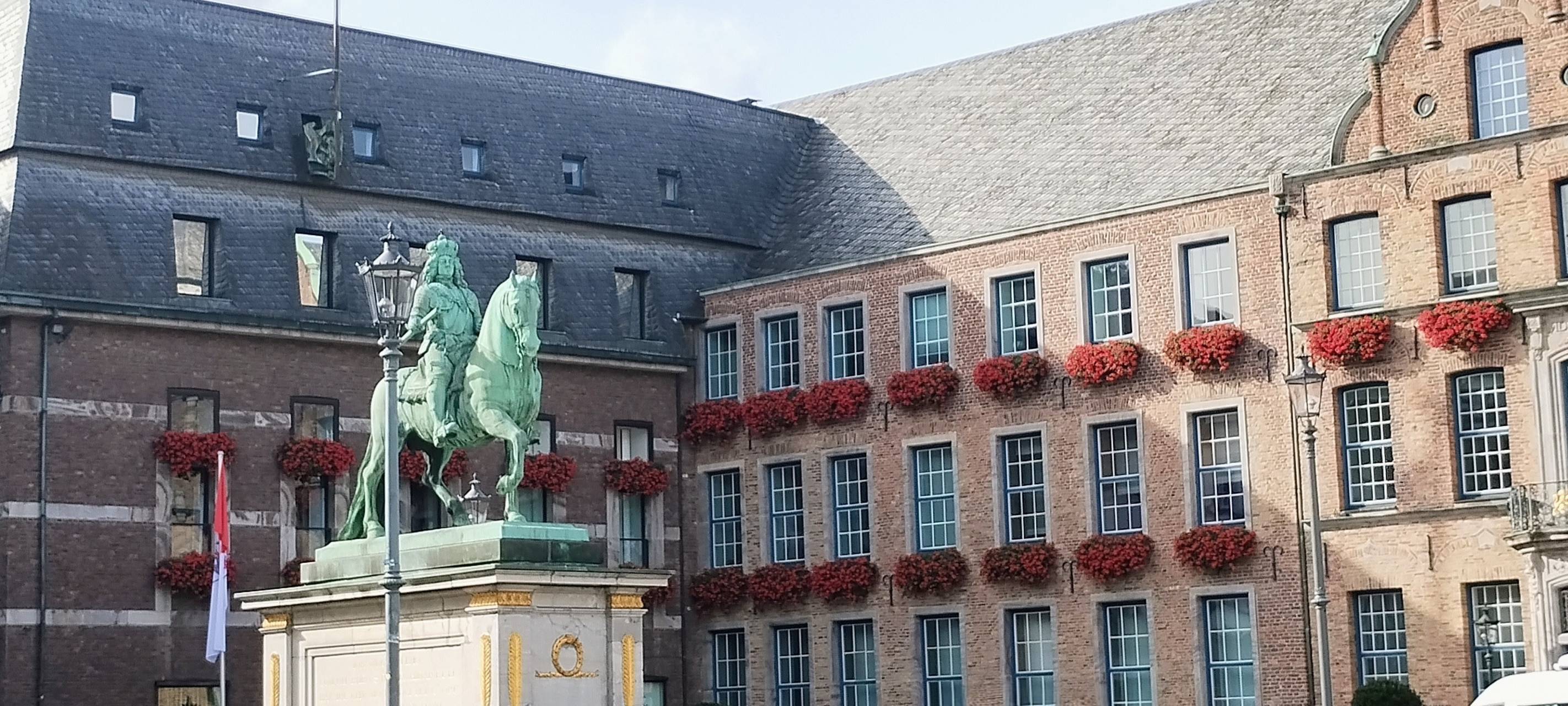 Das Düsseldorfer Rathaus mit bepflanzten Geranienkästen in der Altstadt. Davor steht die Statue von Jan Wellem.
