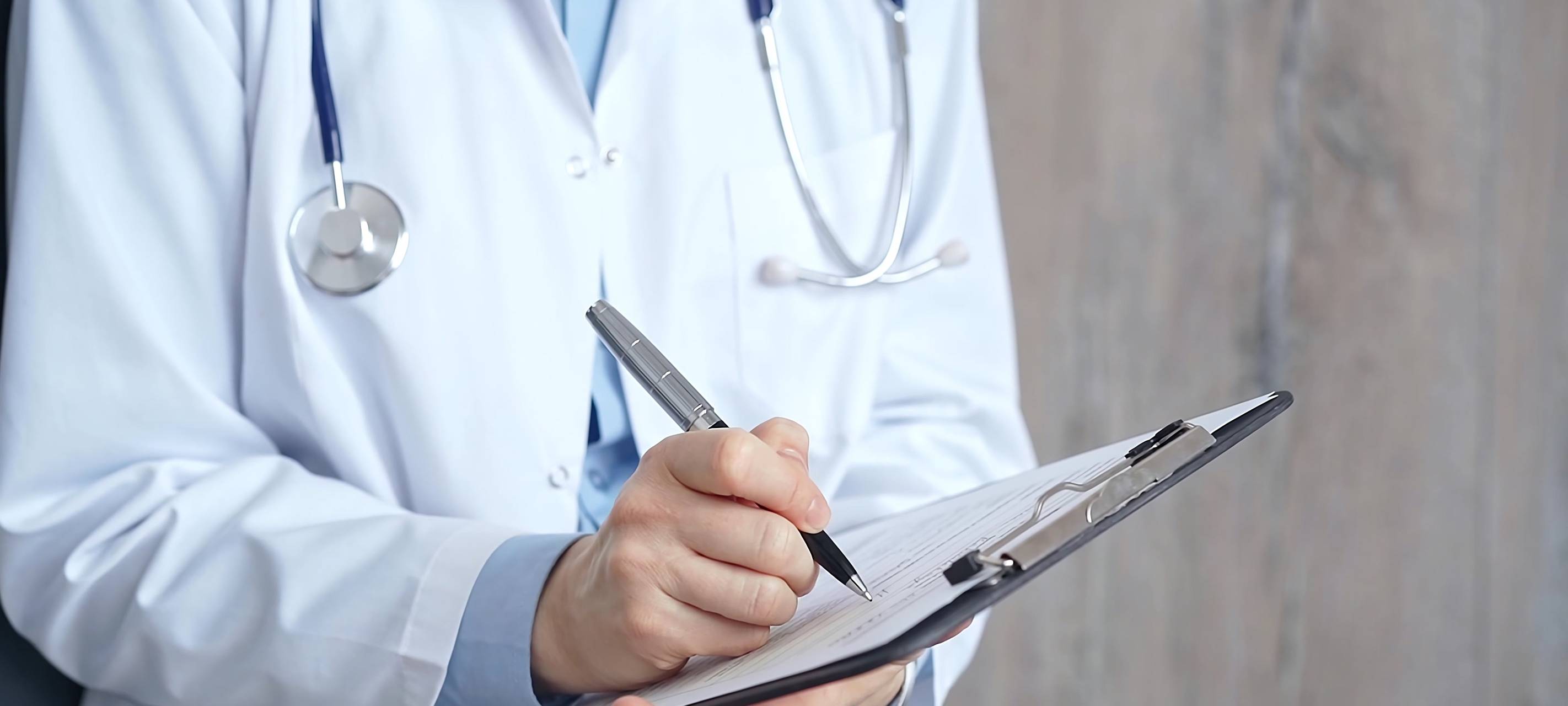 Weibliche Ärztin schreibt medizinische Unterlagen auf ein Klemmbrett, Gesicht nicht erkennbar, Symbolbild für Medizin und Pharmazie.