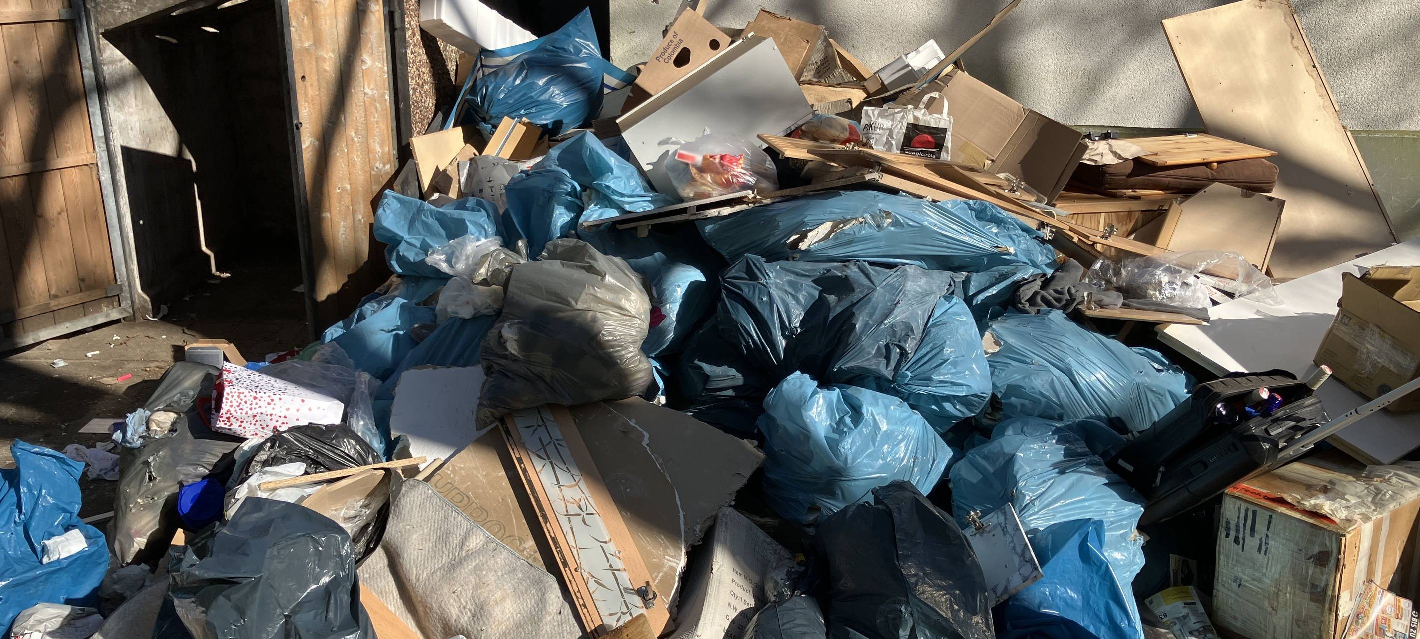 Mehrere Säcke mit Bauschutt liegen in Hassels auf dem Bürgersteig neben anderen abgelagerten Abfällen. Darunter sind Pappkartons, alte Möbel und anderer Müll.