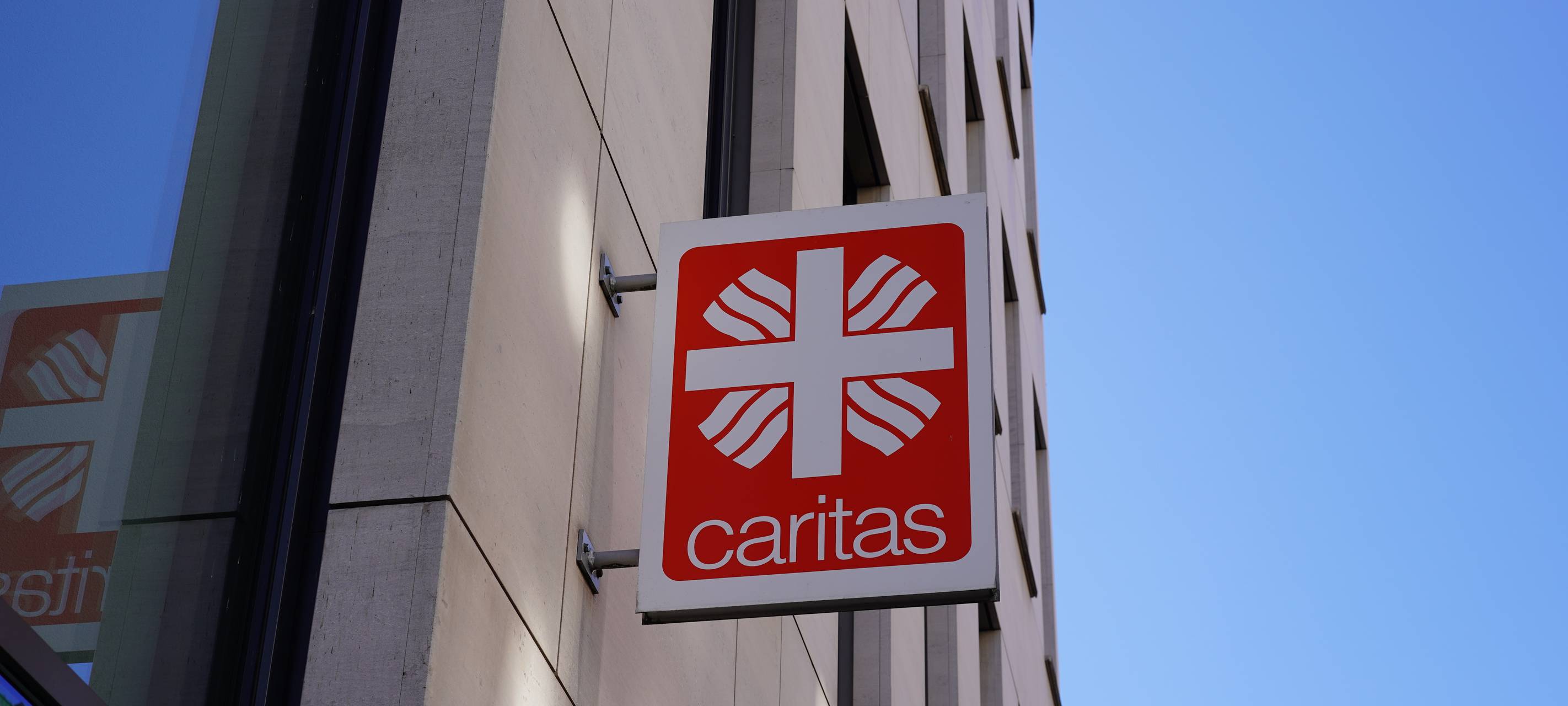 Ein Schild der Caritas hängt an einer Häuserwand. Dieses Bild dient als Symbolbild für die Caritas.