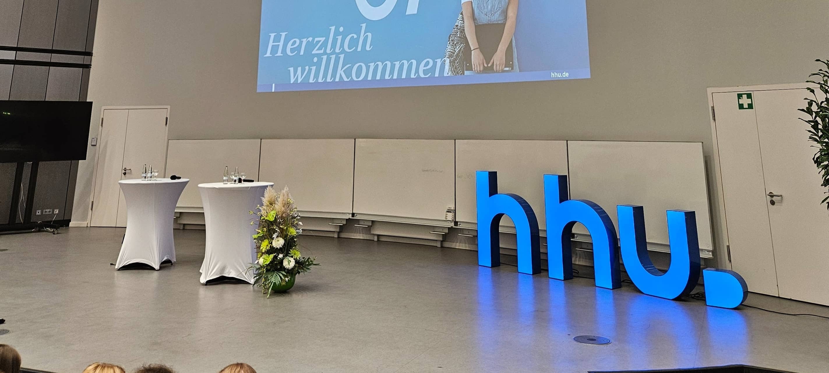 Bühne im Hörsaal 3A der Heinrich-Heine-Universität mit hhu Zeichen auf der rechten Seite.