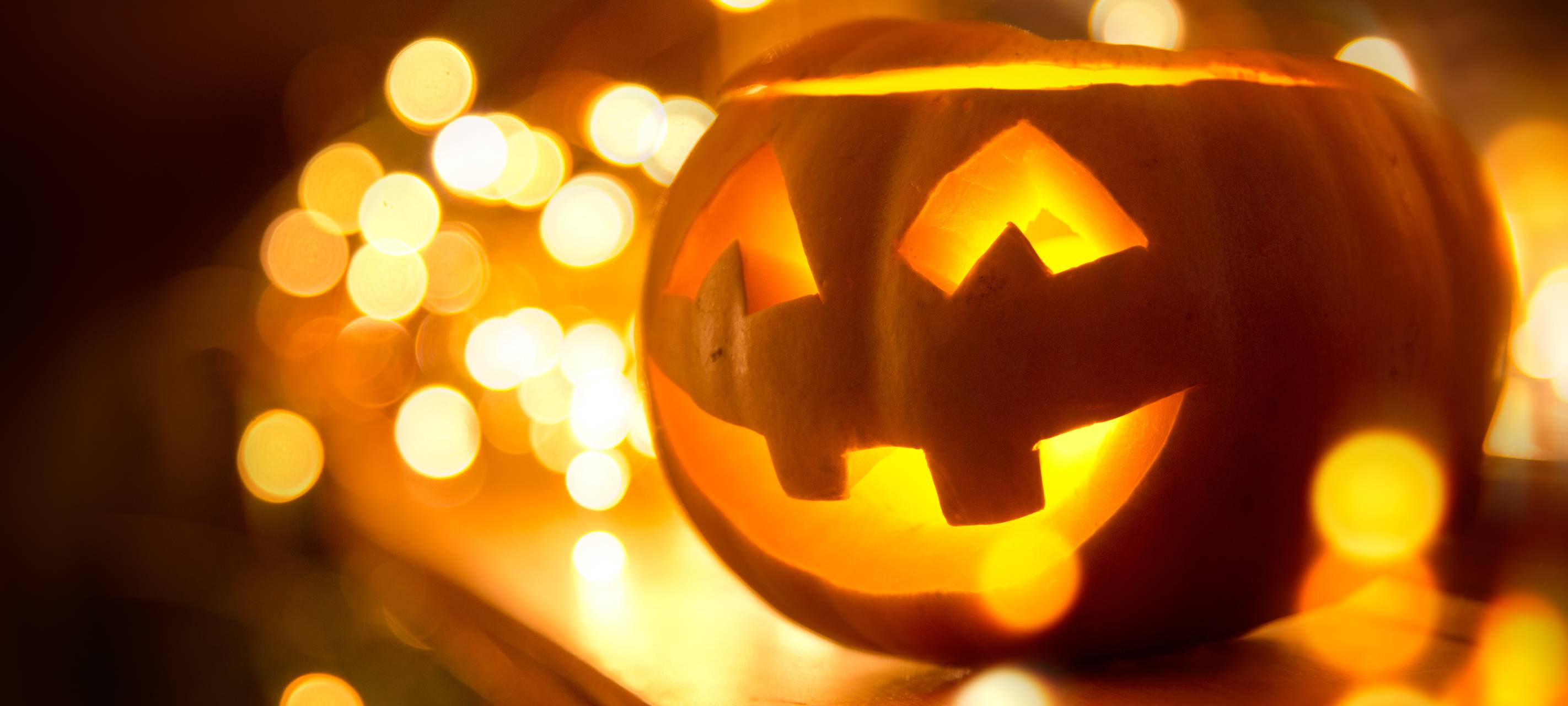 Ein fröhlich lächelnder Jack O’Lantern steht zu Halloween auf einem Kamin, umgeben von Lichterketten.