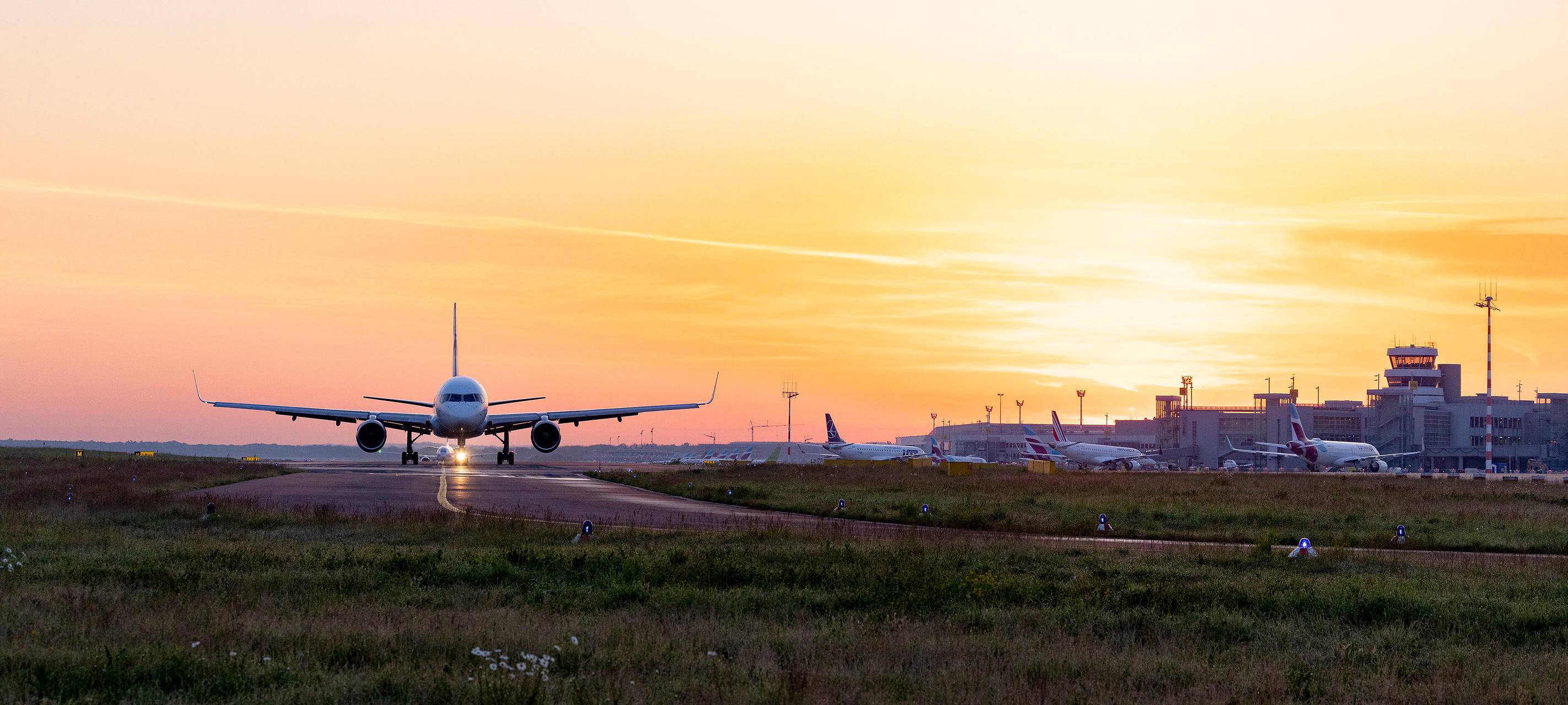 Ein Flugzeug steht auf dem Rollfeld des Düsseldorfer Flughafens vor einem Sonnenuntergang oder -aufgang.