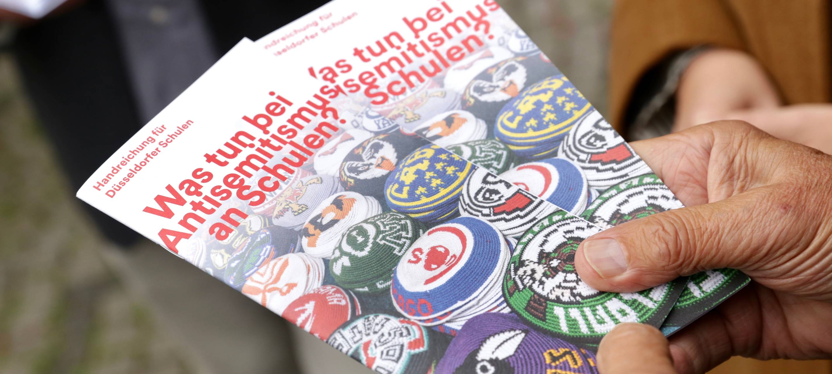 Zwei Hände halten zwei Exemplare der Broschüre "Was tun bei Antisemitismus?" in die Kamera