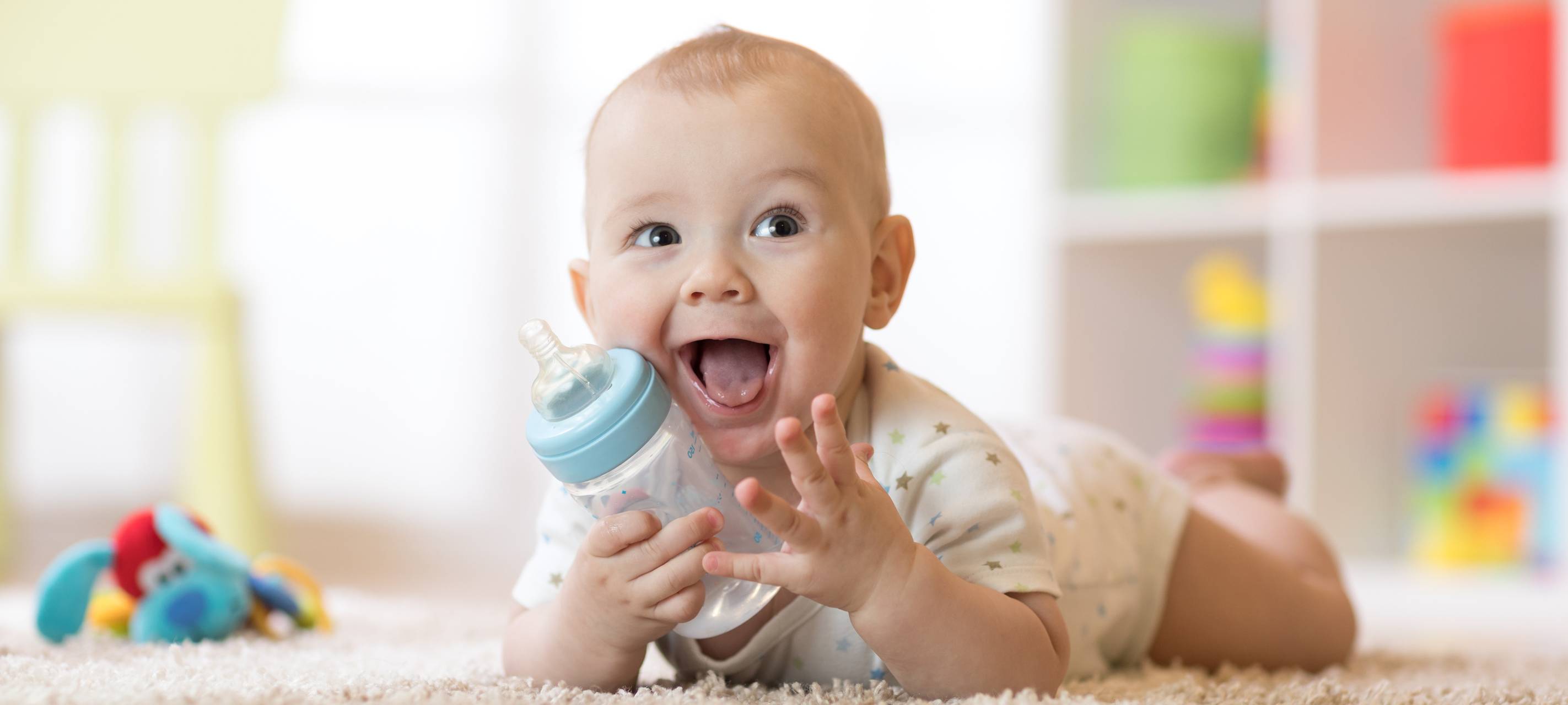 Lächelnder Säugling (7 Monate alt) trinkt aus einer Babyflasche.