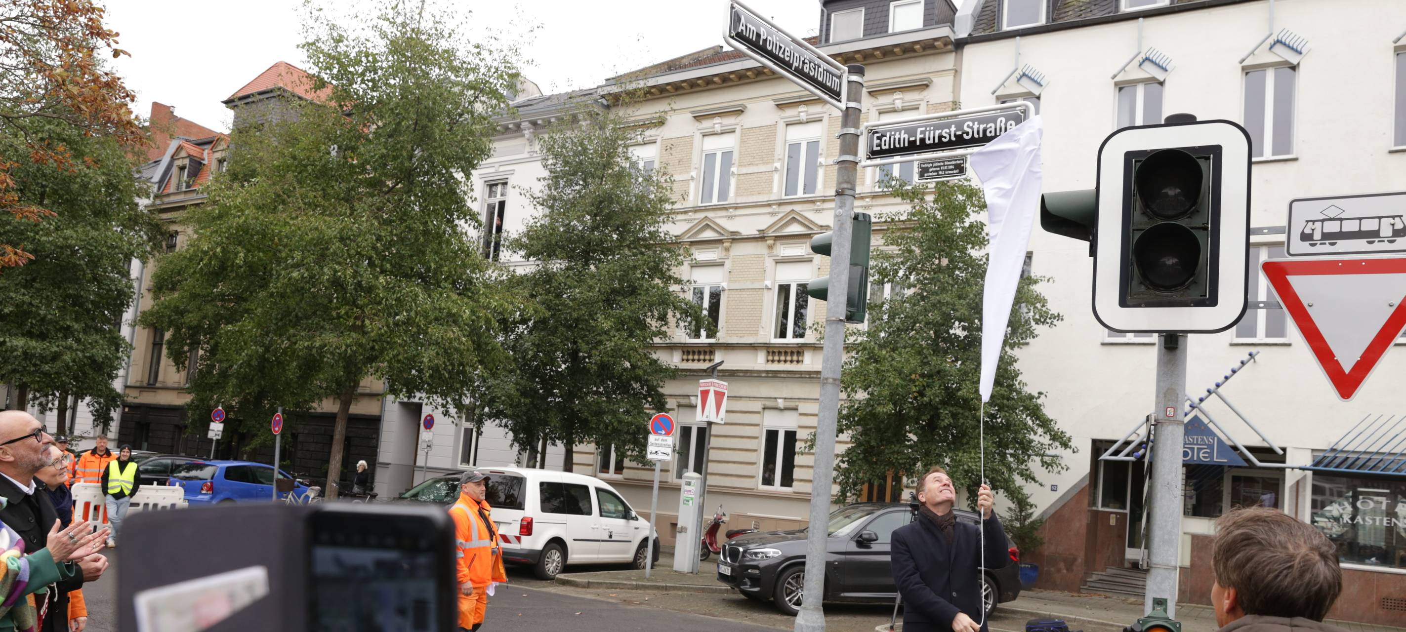OB Keller enthüllt die neuen Straßenschilder "Am Polizeipräsidium" und "Edith-Fürst-Straße". Viele Nachbarn und Fotografen beobachten die Aktion auf dem ehemaligen Jürgensplatz.