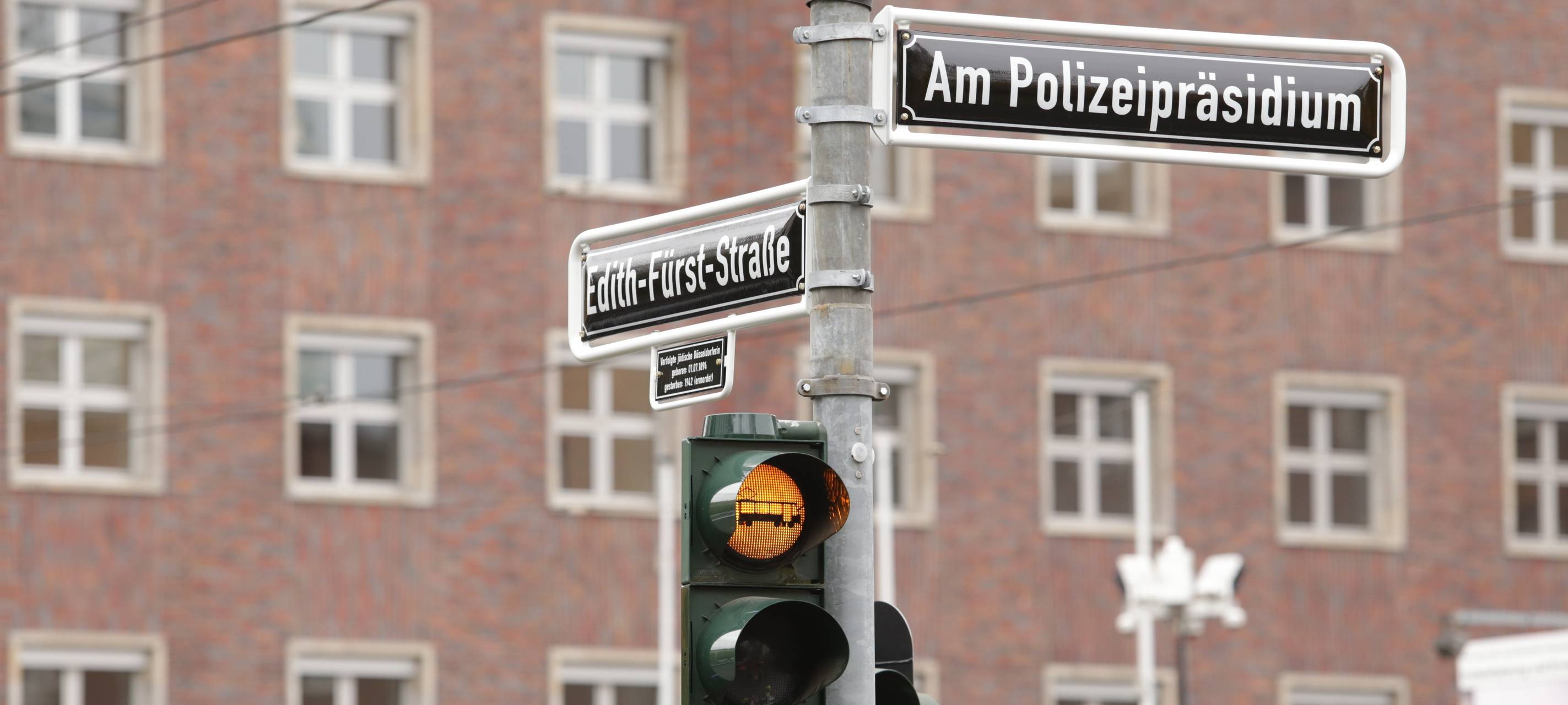Vor dem Polizeipräsidium steht ein Ampelmast, der auf eine Straßenbahn hinweist. An dem Mast auf dem ehemaligen Jürgensplatz hängen außerdem die neuen Straßenschilder "Am Polizeipräsidium" und "Edith-Fürst-Straße"