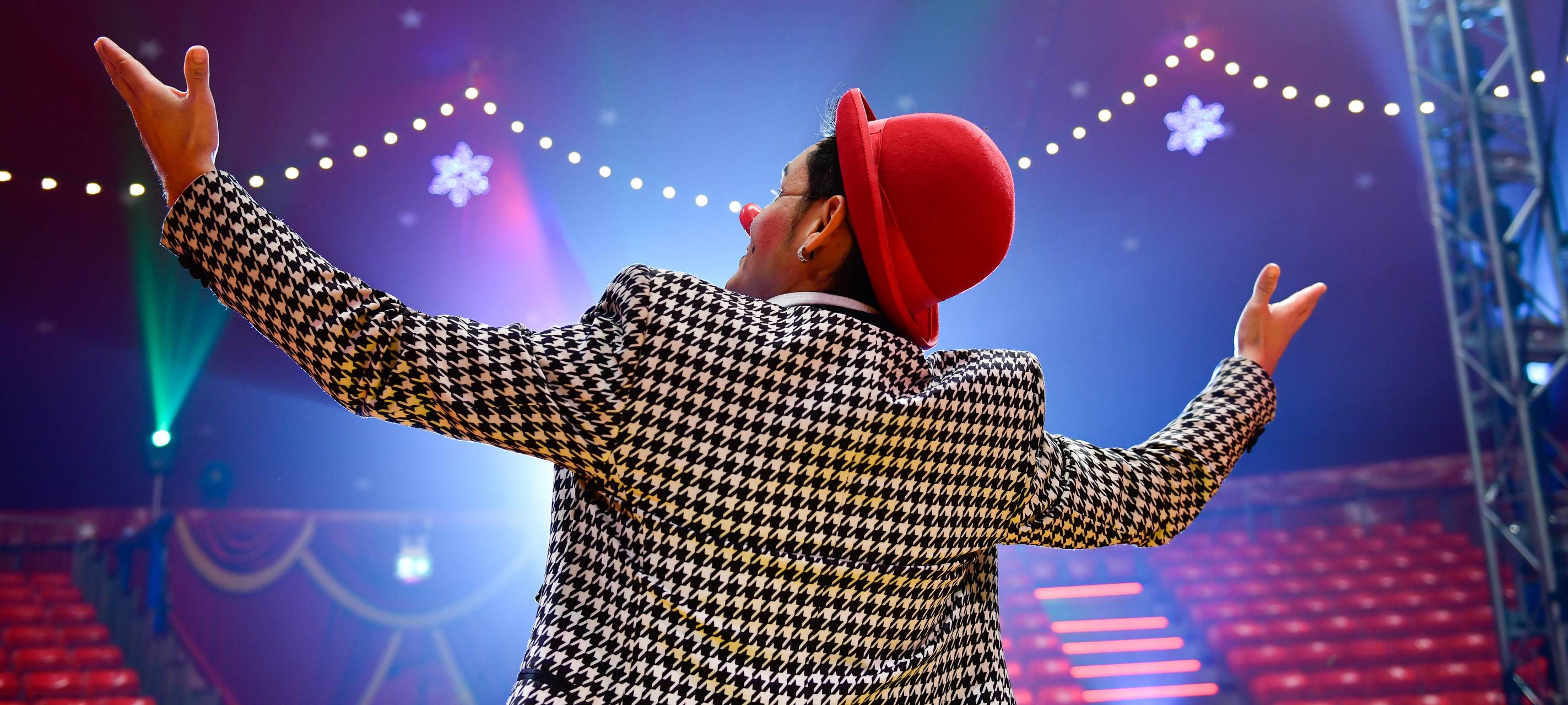 Ein Clown steht in der Manege und breitet die Arme aus, man sieht ihn von hinten