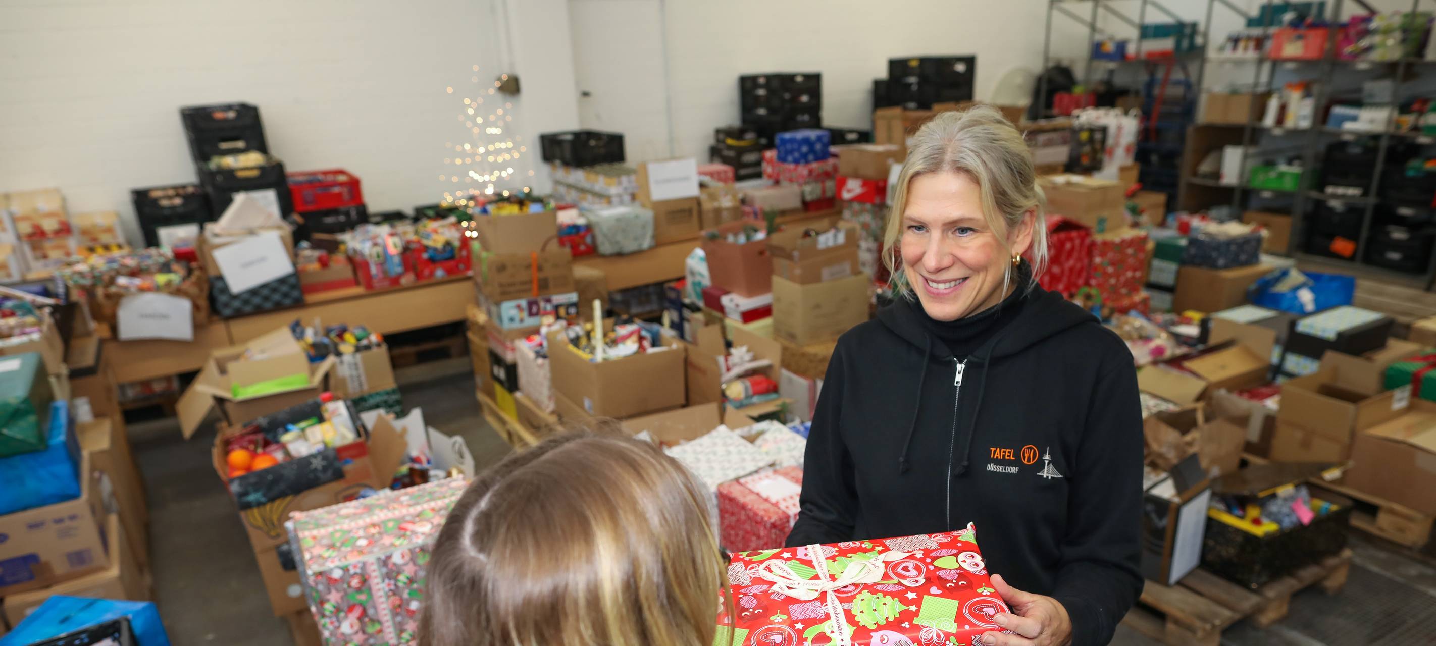 Eine Frau übergibt ein Weihnachtspaket an eine Frau der Tafel Düsseldorf. Die Tafel sammelt Päckchen für von Armut betroffenen Düsseldorfern.