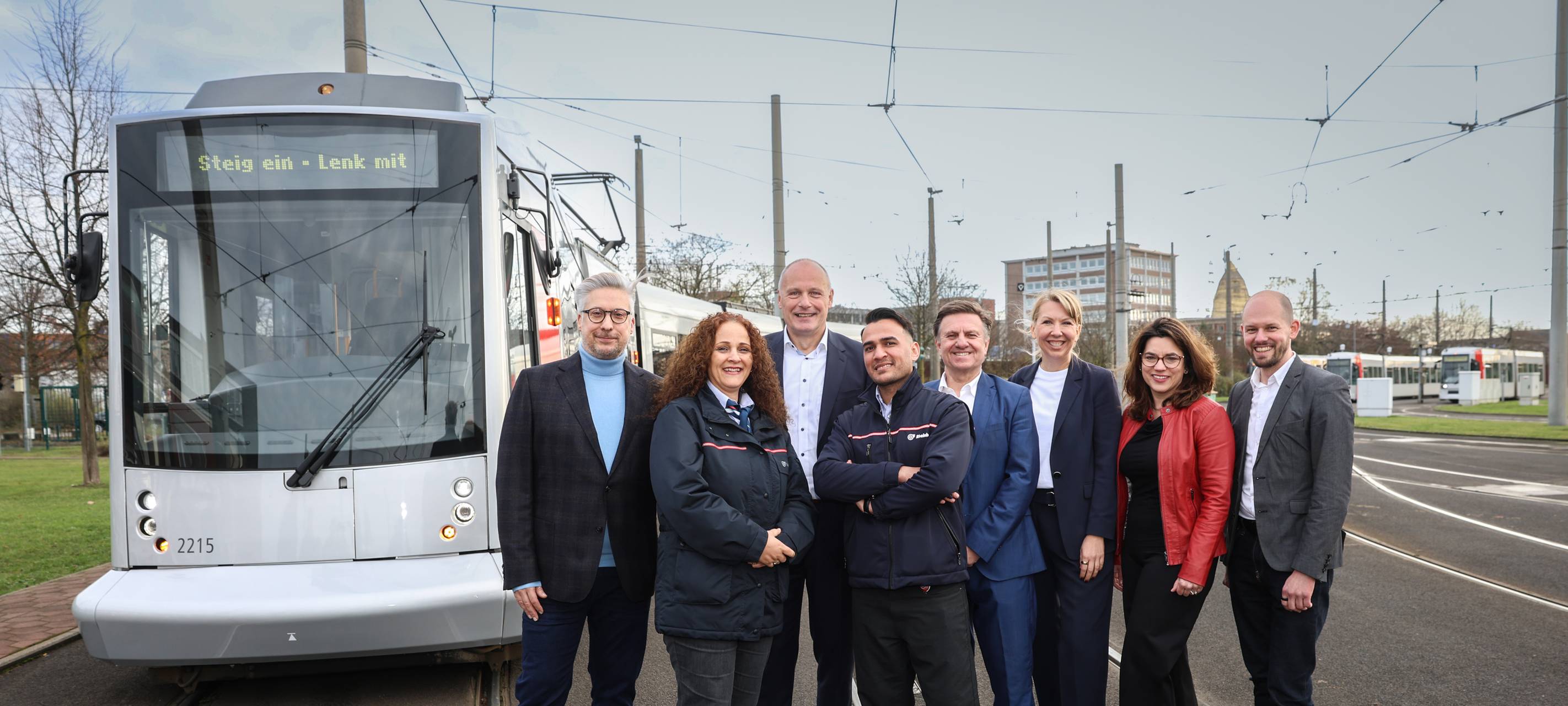 Beteiligten des Projekts „Steig ein – Lenk mit!" stehen vor einer Straßenbahn der Rheinbahn auf den Schienen.