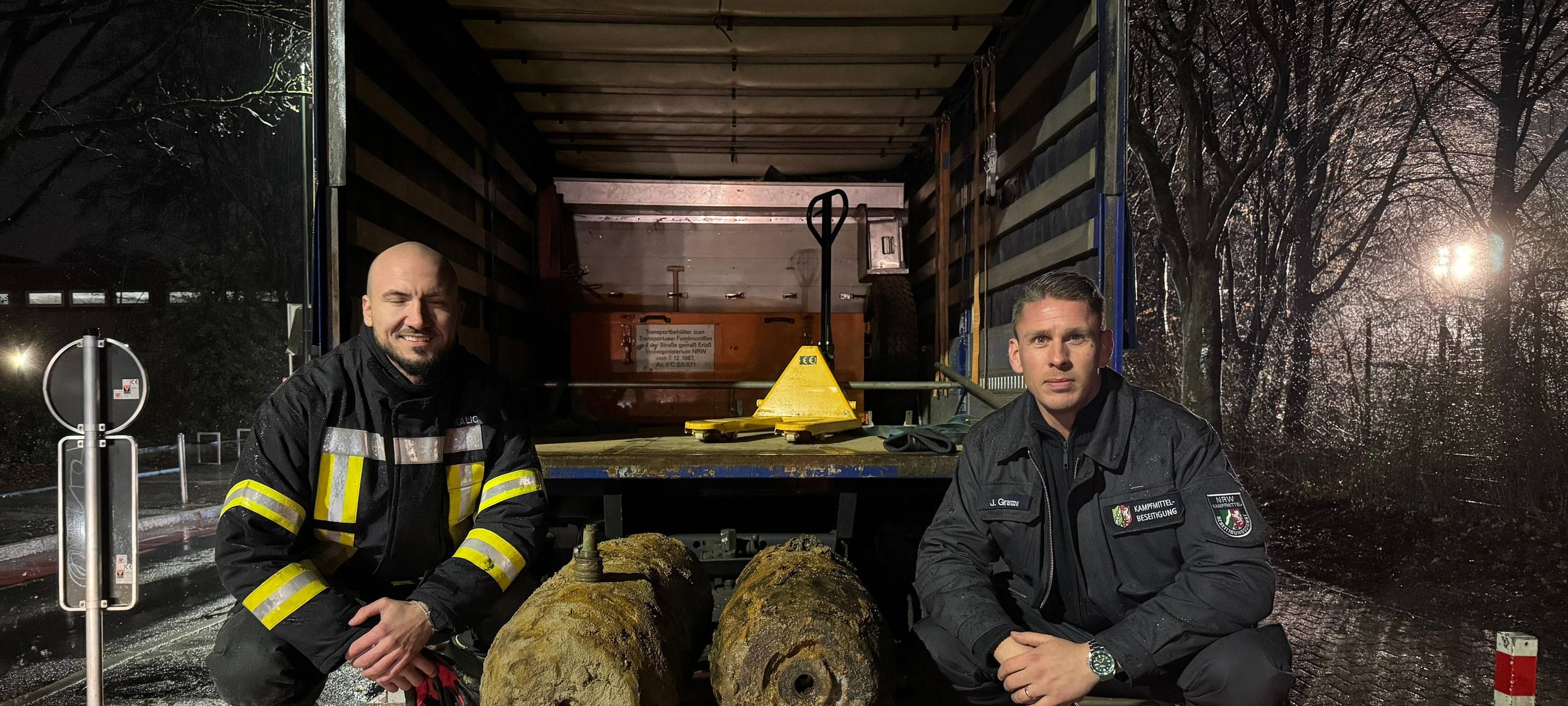 ein Feuerwehrmann und ein Polizist hocken links und rechts neben zwei entschäften Fliegerbomben aus dem zweiten Weltkrieg.