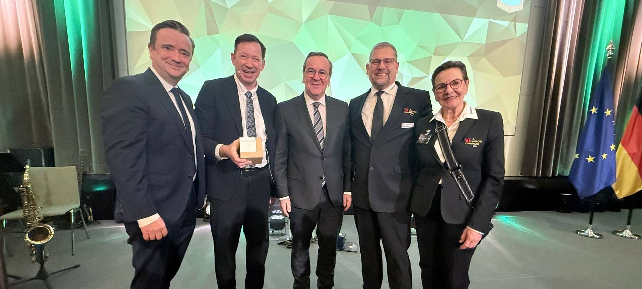 Vier Männer und eine Frau stehen auf einer Bühne und schauen lächelnd in die Kamera. Einer der Männer hält einen Preis in der Hand.