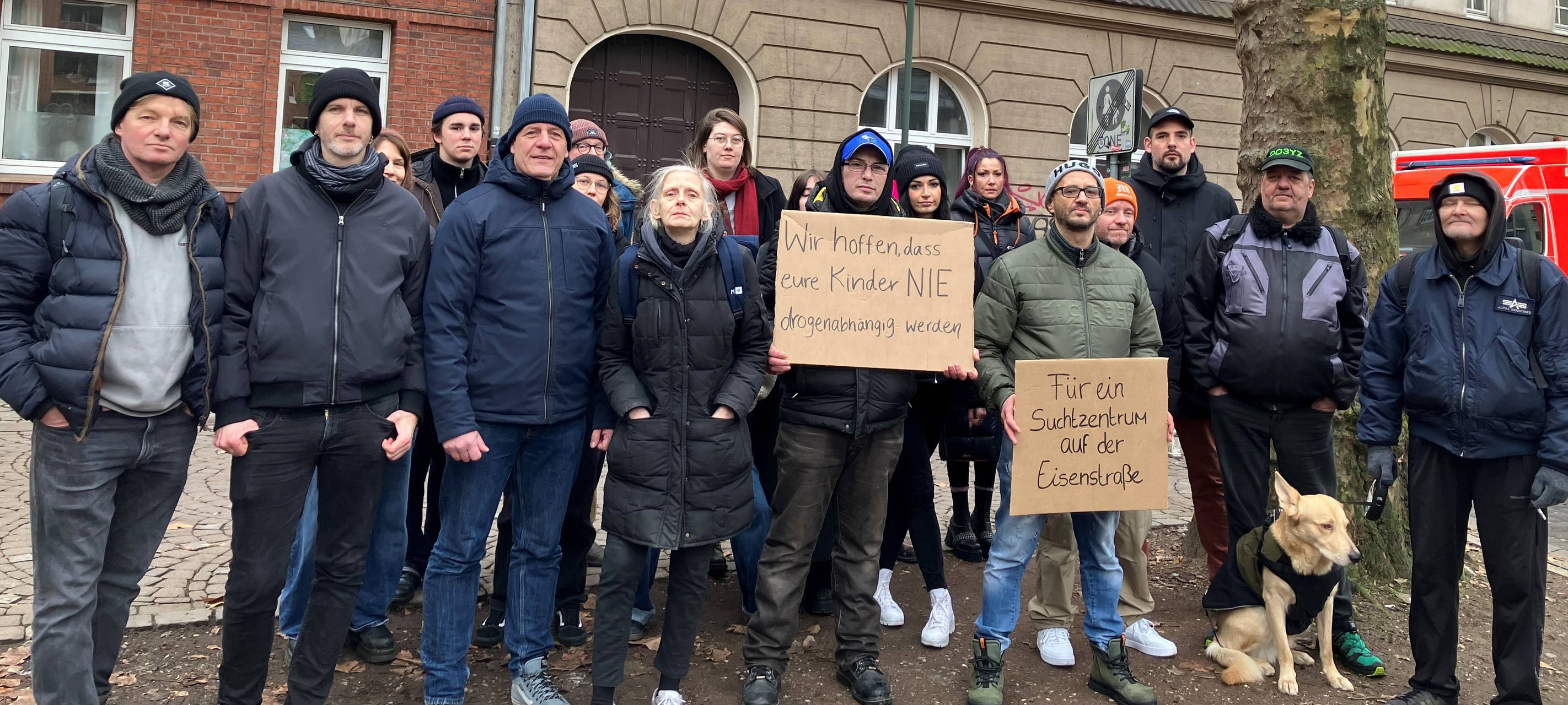 Eine Gruppe Menschen steht vor einem Gebäude. Einige halten Schilder in der Hand. Darauf steht "Für ein Suchtzentrum auf der Eisenstraße".