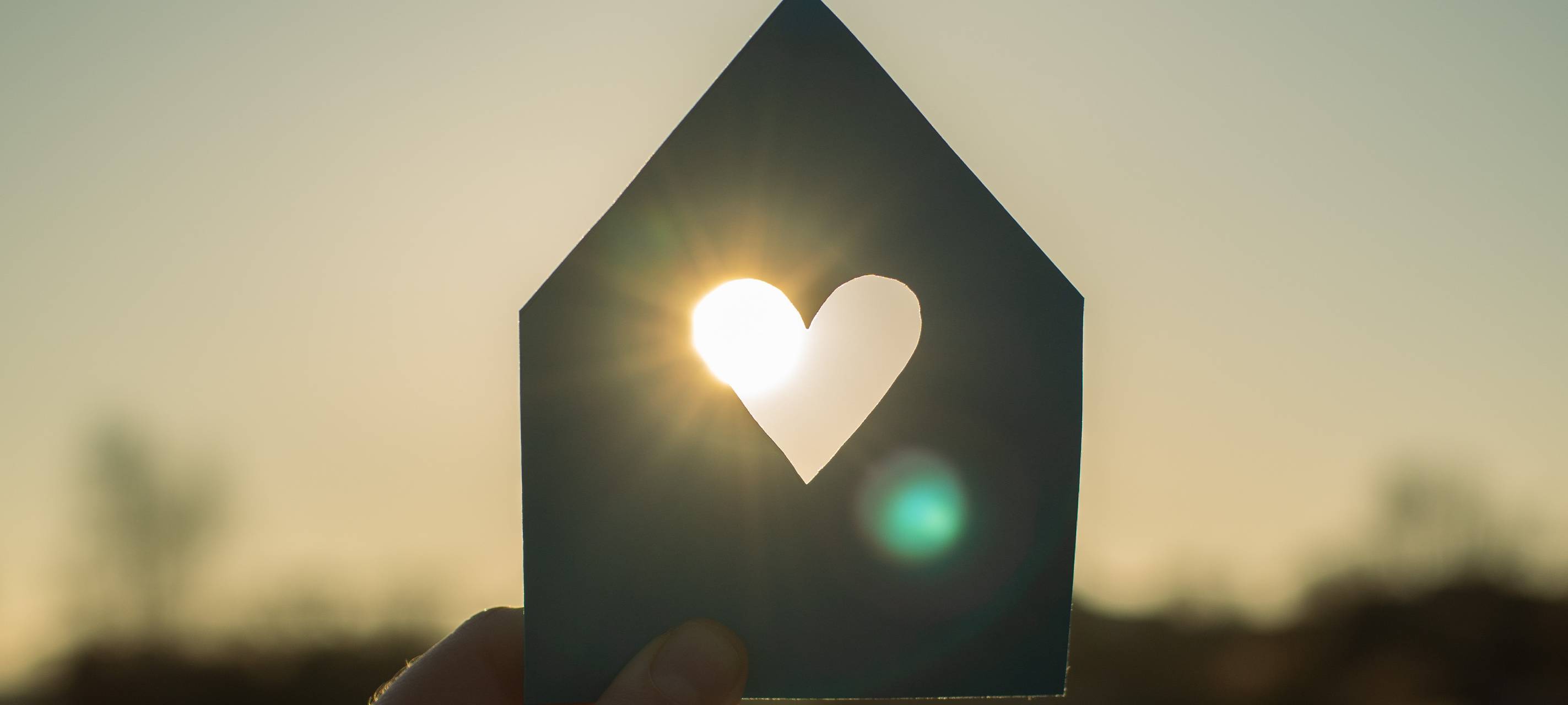 Eine Hand hält ein Papphaus vor die Sonne, in dessen Mitte ein Herz ausgeschnitten wurde.