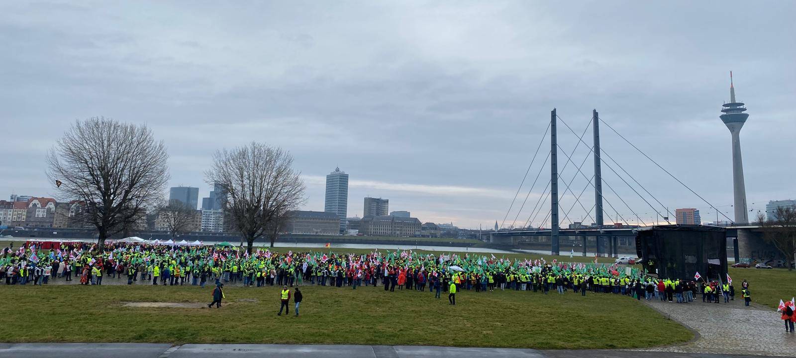Eine Menschenmenge versammelt sich am Rheinufer vor einer Bühne zu einer Kundgebung der Gewerkschaft Verdi.
