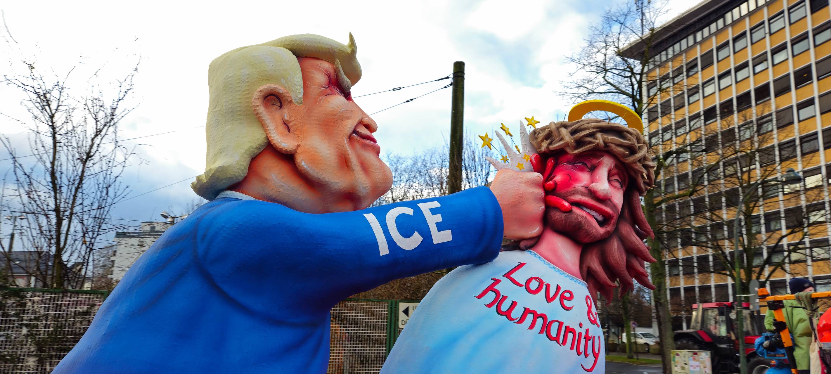 Motivwagen: Trump mit dem Schriftzug "ICE" versehen schlägt Jesus der auf der Brust "Love & Humanity" stehen hat